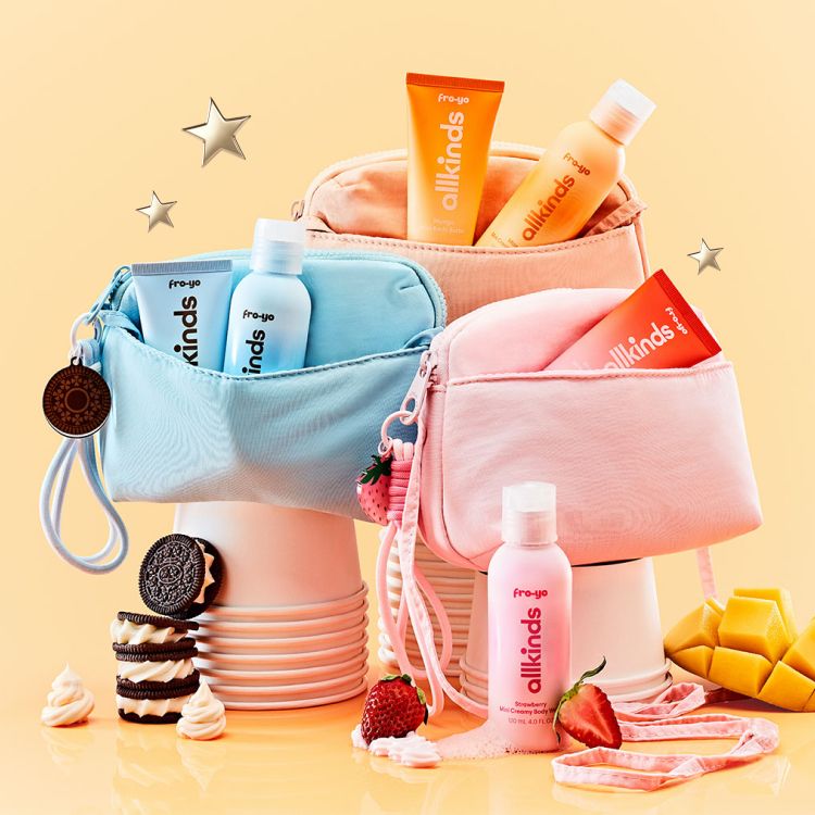 Pastel blue, orange, and pink Fro-go Allkinds cosmetic pouches hold matching products, surrounded by Oreos, strawberries, and mango.