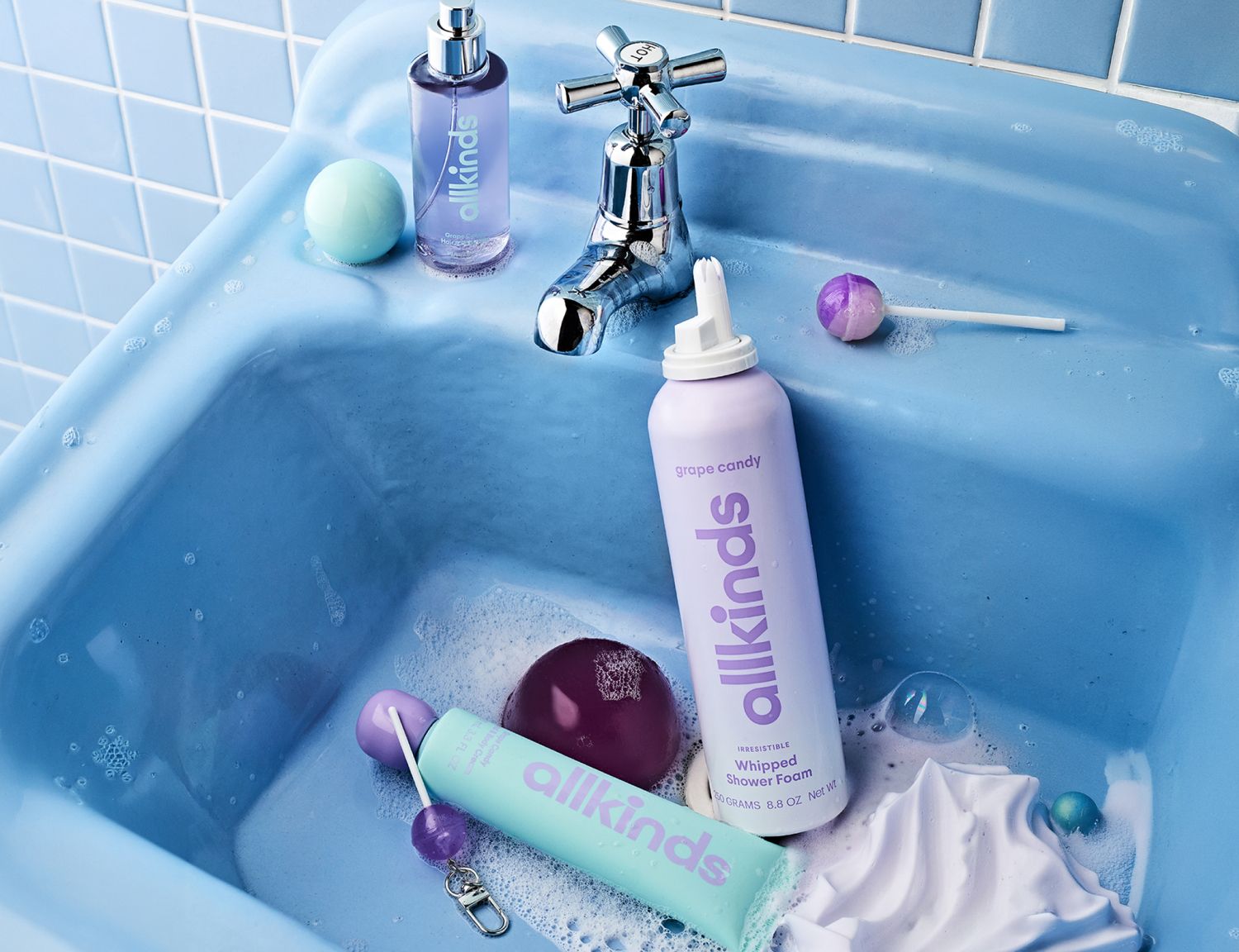 allkinds bath products and candies in pastel purple, blue, and green shades sit in a bubbly blue sink.