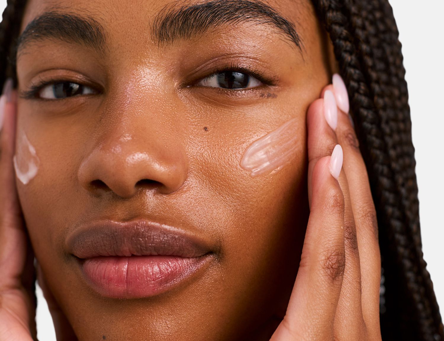 Close-up of a person with dark skin applying a translucent gel to their cheeks, showing visible streaks.