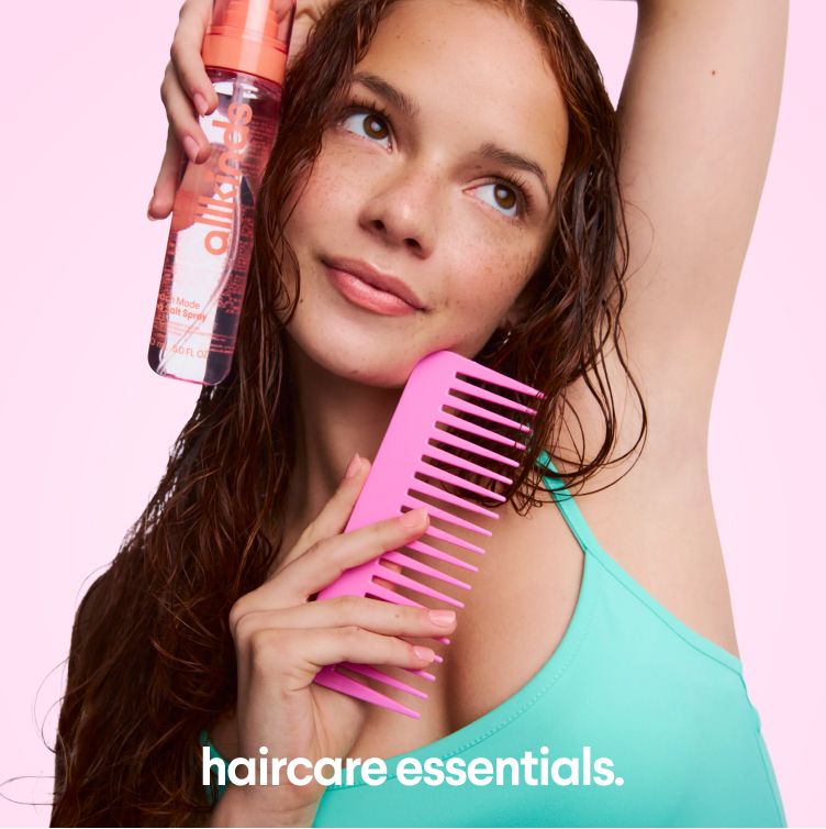 A woman with wet, wavy hair holds a hair product bottle and a pink wide-tooth comb; text reads "haircare essentials."