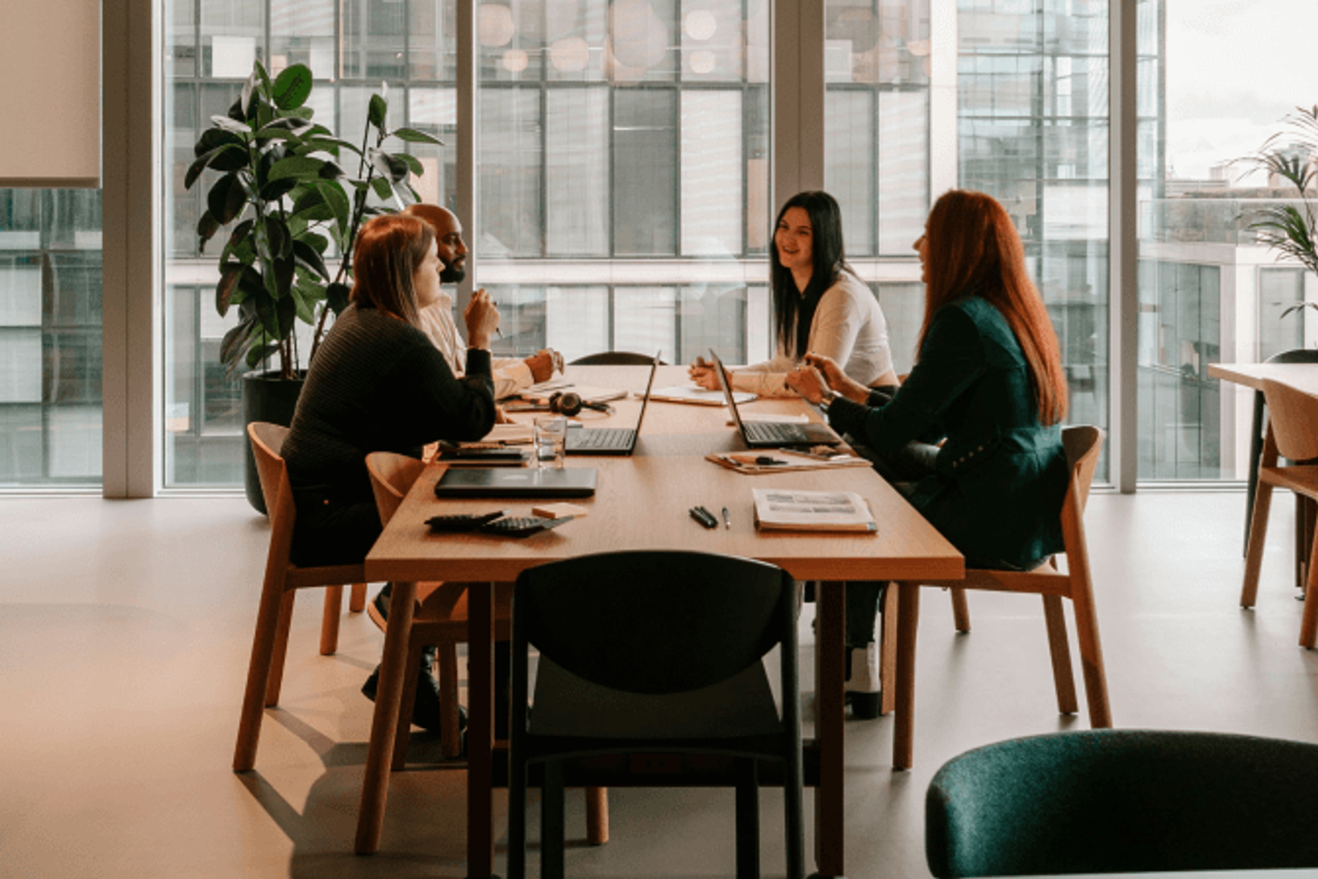 Four colleagues collaborating at a table in a modern glass-walled office