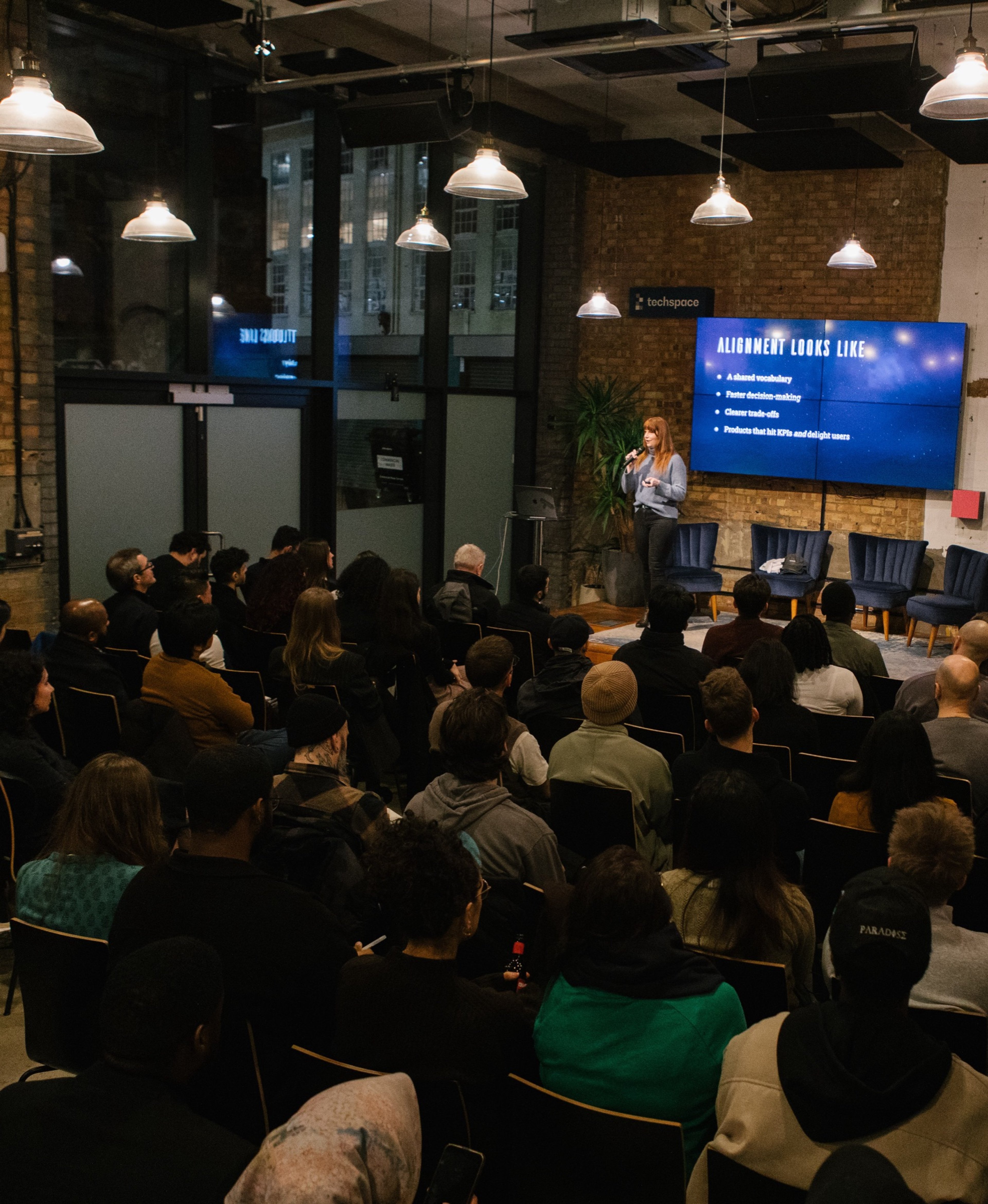 A full audience watching a speaker present at INTERFACE in a brick-walled venue