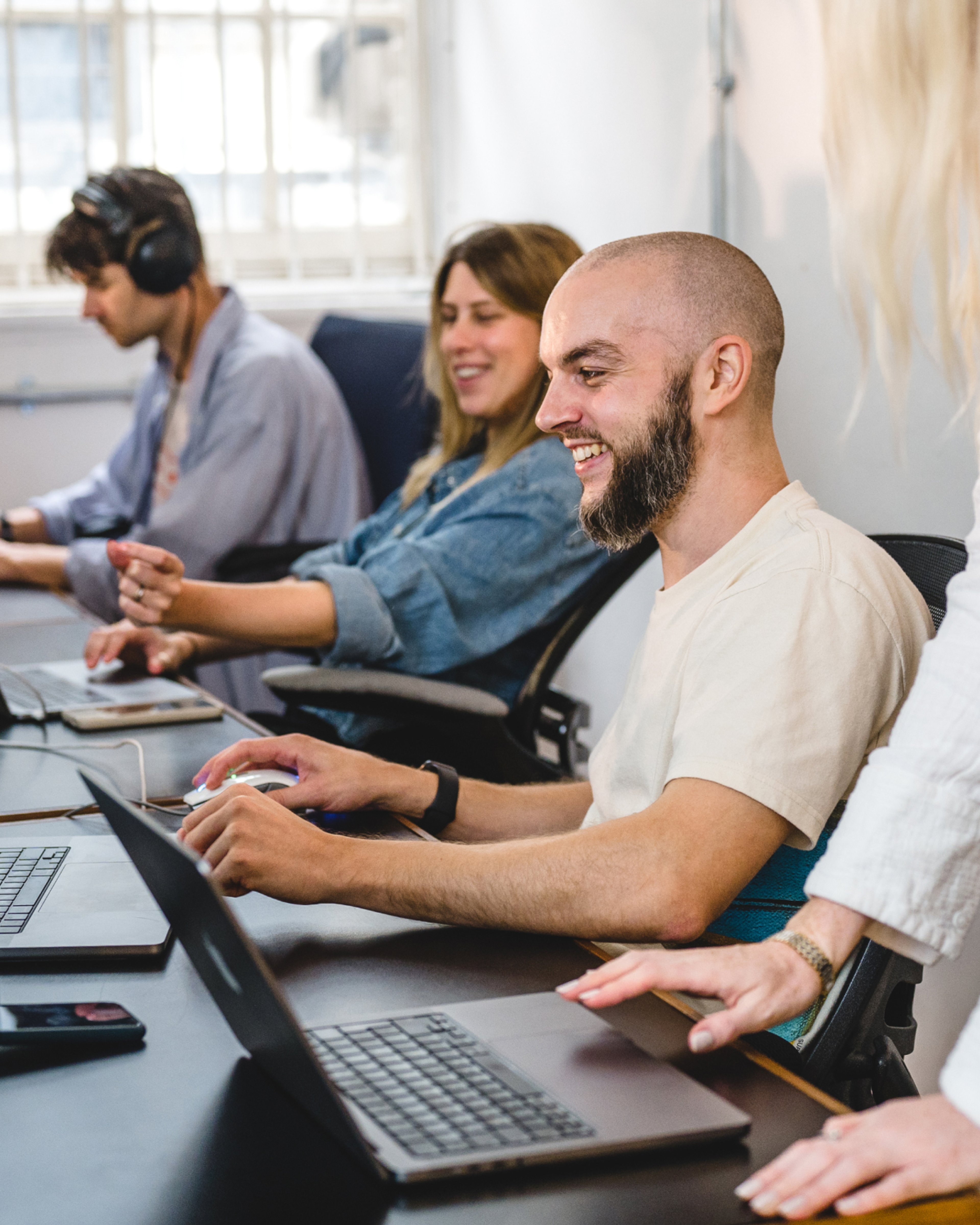A row of team members working on laptops along a shared desk, one smiling in the foreground. North Star concept development, Research & Strategy.