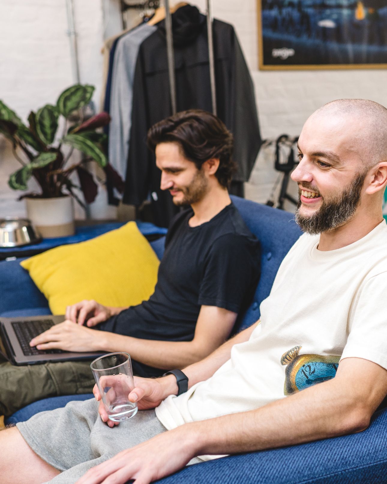 Two team members chatting on a sofa, one working on a laptop. Software Engineering.