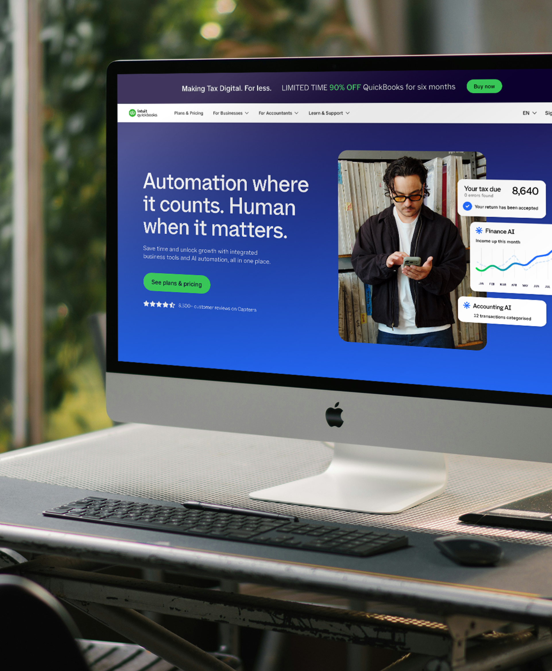 An iMac on a desk showing the redesigned QuickBooks homepage