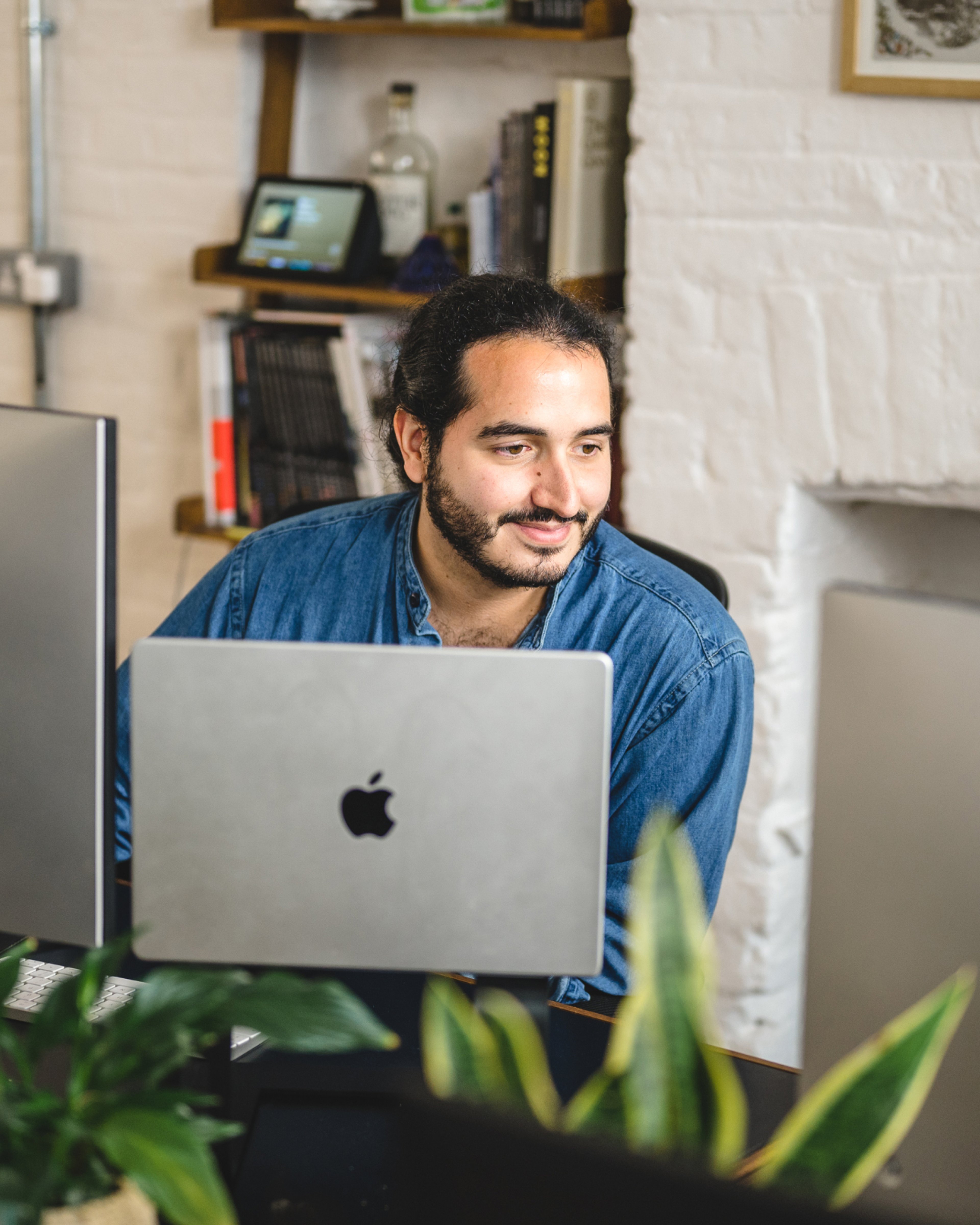 A team member smiling behind a laptop at a desk with plants and a bookshelf. Conversion rate optimisation (CRO), Experience Design.