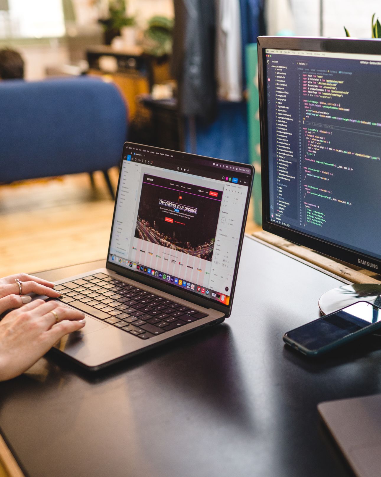 Code on a desktop monitor beside a laptop showing a website. Bespoke CMS development, Software Engineering.