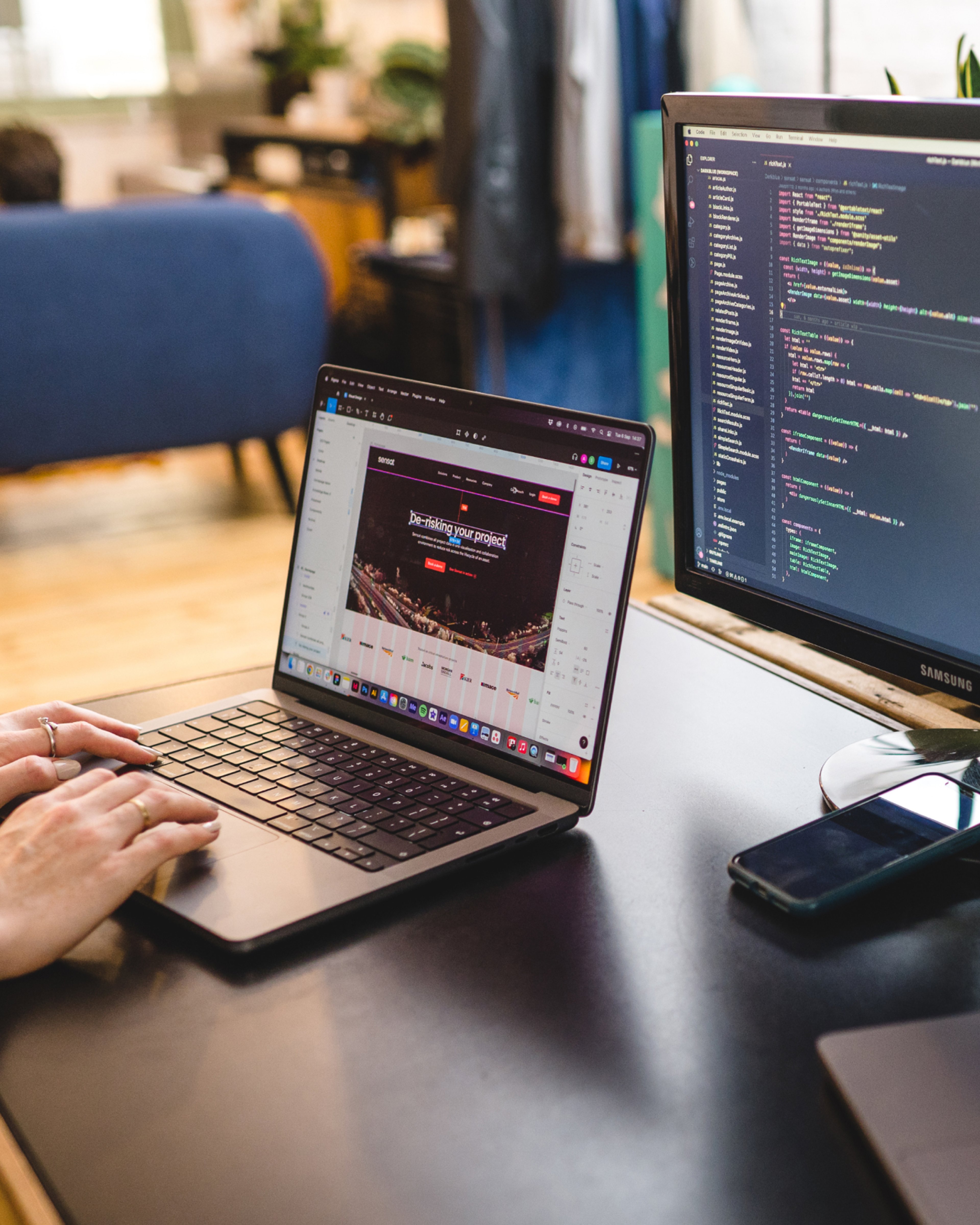 Code on a desktop monitor beside a laptop showing a website. Bespoke CMS development, Software Engineering.