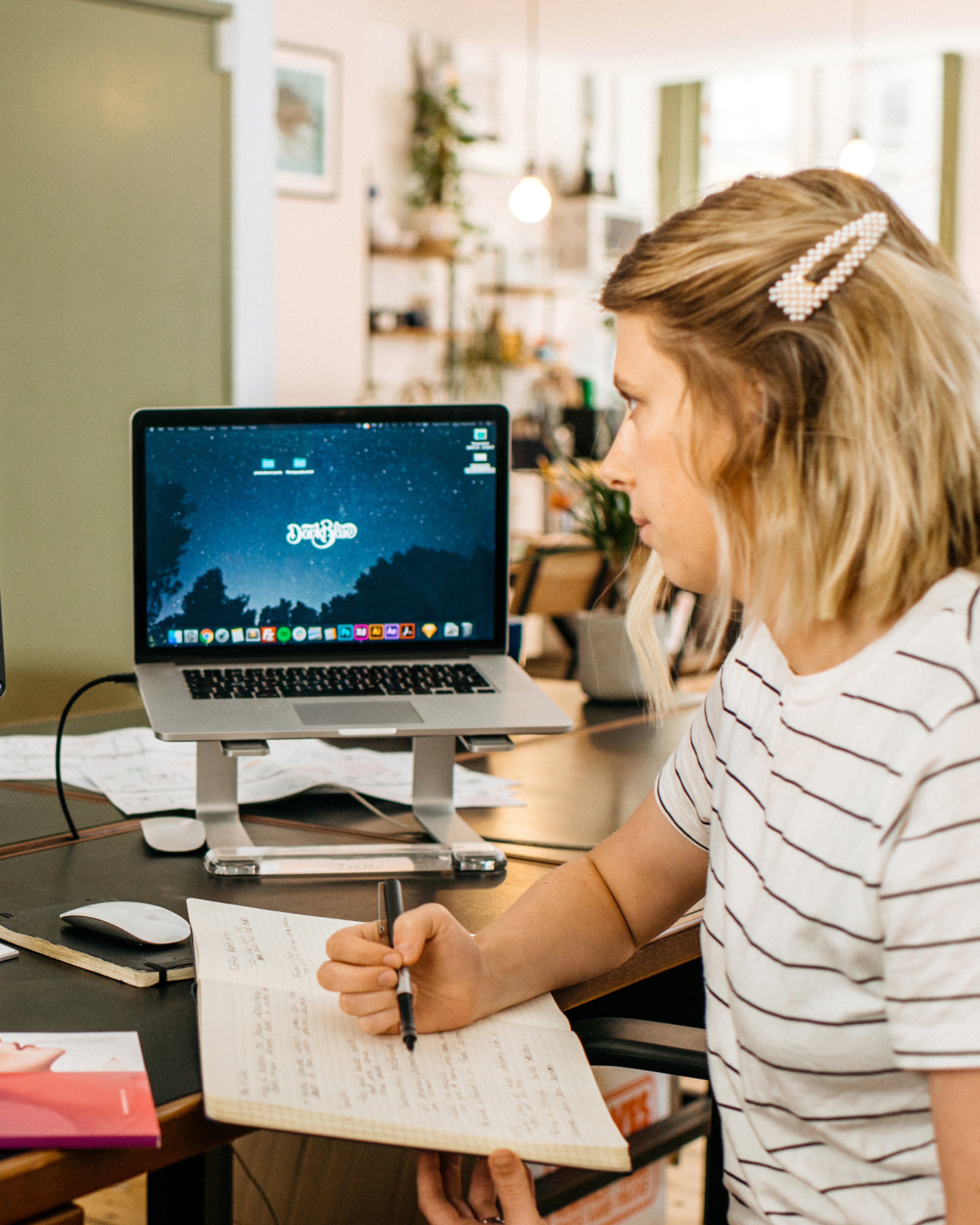 A team member writing notes beside a laptop on a stand. AI search visibility, AI & Emerging Technology.