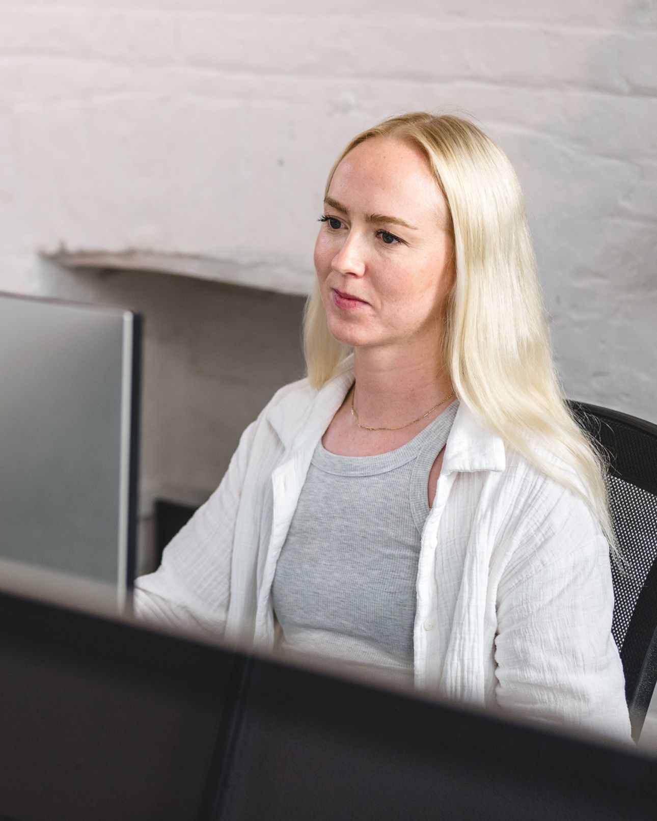 A team member working at a computer in the studio, in front of a whitewashed brick wall. Research & Strategy.