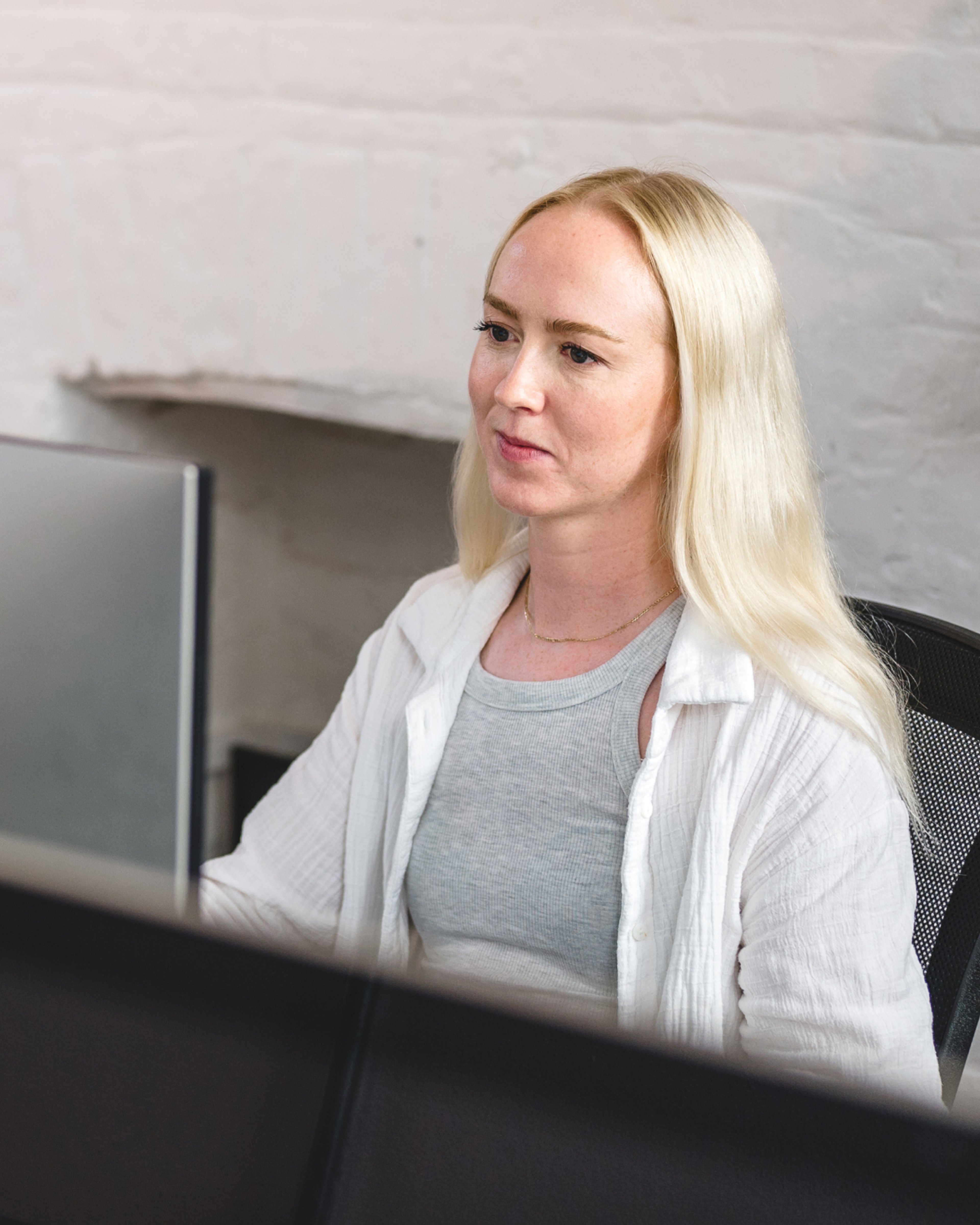 A team member working at a computer in the studio, in front of a whitewashed brick wall. Research & Strategy.