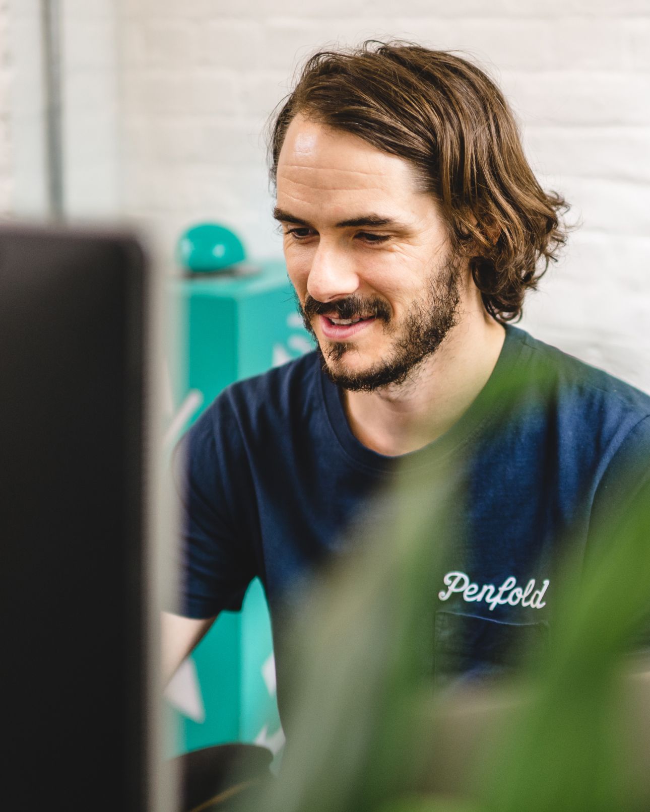A team member smiling at their screen, a plant blurred in the foreground. UX and Information Architecture, Experience Design.