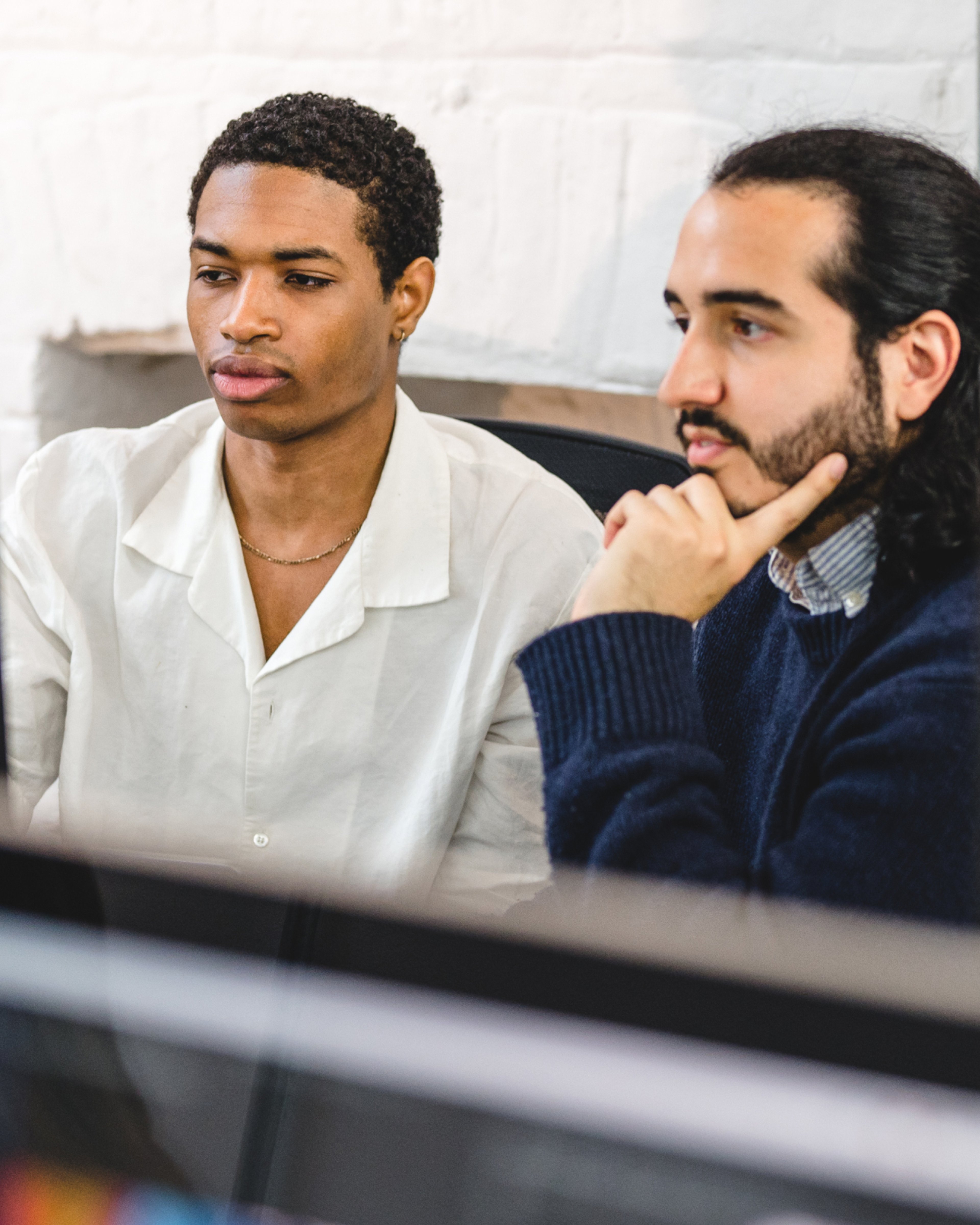 Two team members studying a screen together, one resting their chin on their hand. Product design, Experience Design.