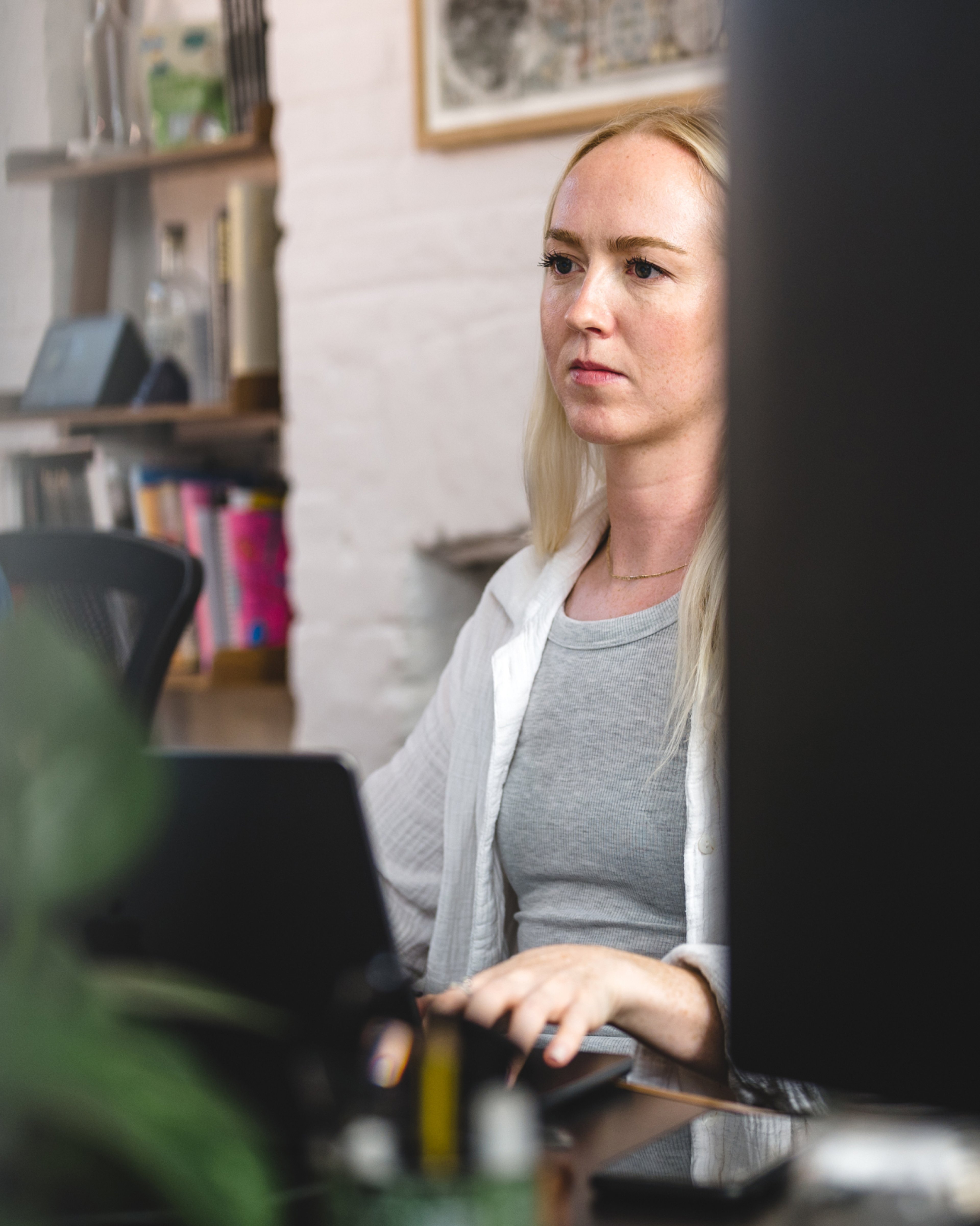A team member focused on a laptop at a desk beside a bookshelf in the studio. Audience research, Research & Strategy.