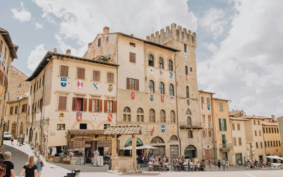 Piazza Grande ad Arezzo: palazzo medievale e torre merlata con gli stemmi sopra i tavolini dei caffè.