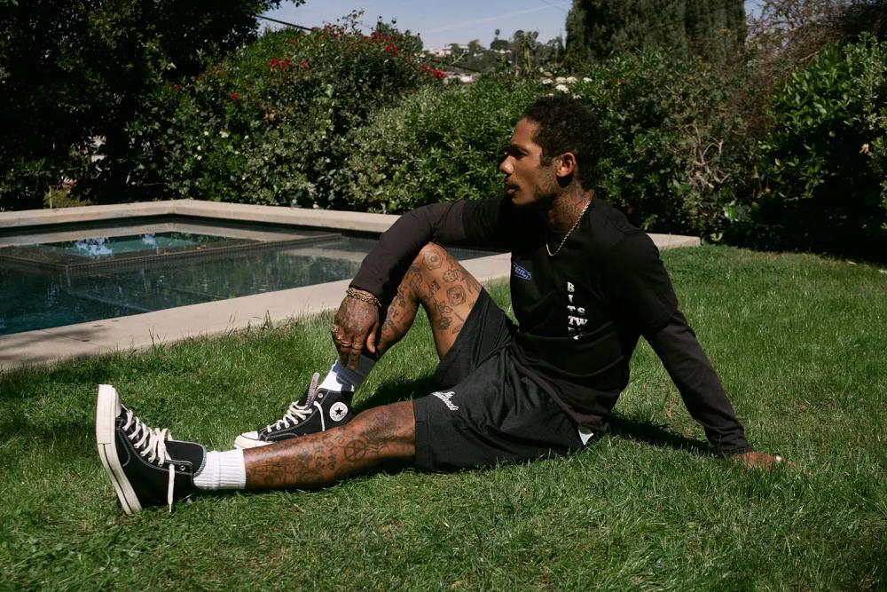 Stylish man in a black t-shirt, black shorts, and black Converse sneakers sitting on the grass Stylish man in a black t-shirt, black shorts, and black Converse sneakers sitting on the grass