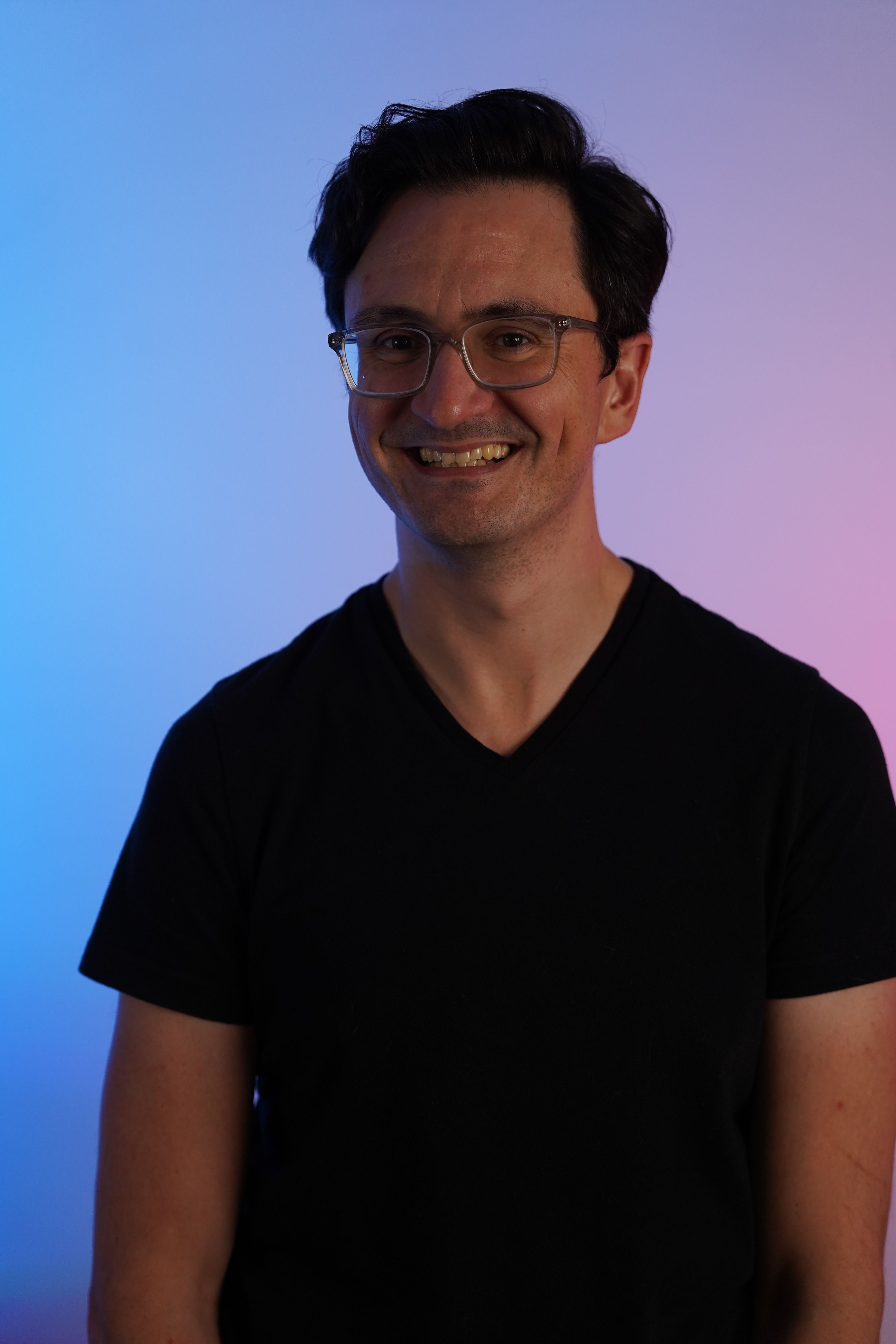 a man wearing glasses and a black shirt smiles for the camera