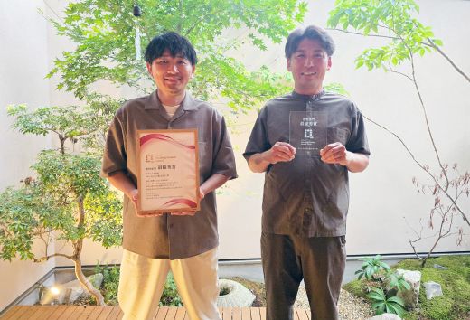 賞状を持った男性と、トロフィーを持った男性がにこやかに笑っている写真