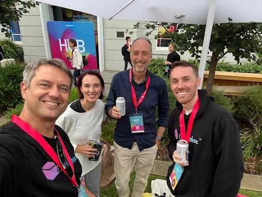 Travis Clapp taking a selfie with Alex Hey and guests at an outdoor event, all wearing event lanyards