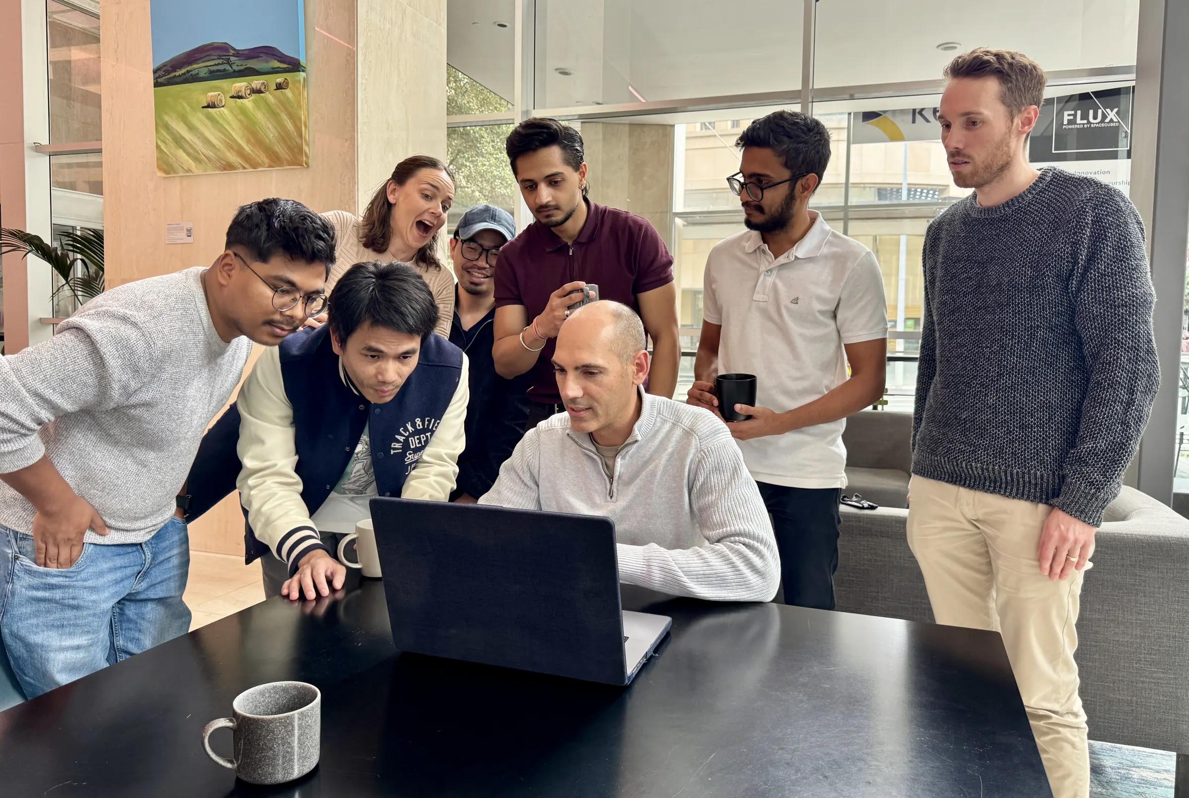 Coursebox AI teammates gathered around a laptop during a live demo at the weekly team meeting