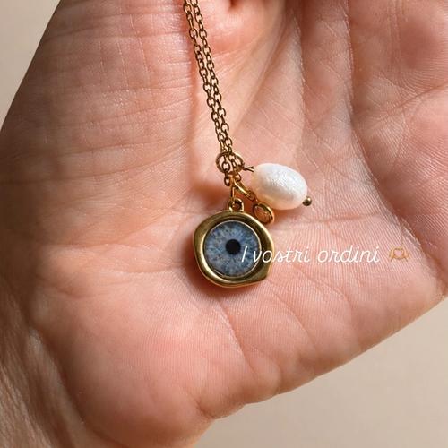 Ciondolo con iride azzurra e perla tenuto in mano