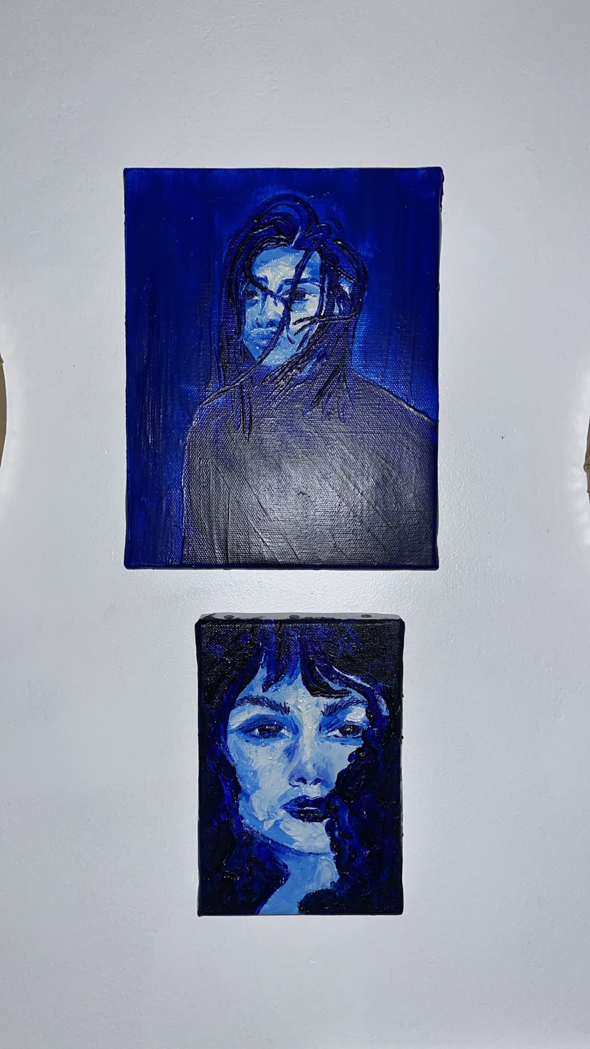 Deux portraits bleus accrochés l’un au-dessus de l’autre sur un mur blanc.