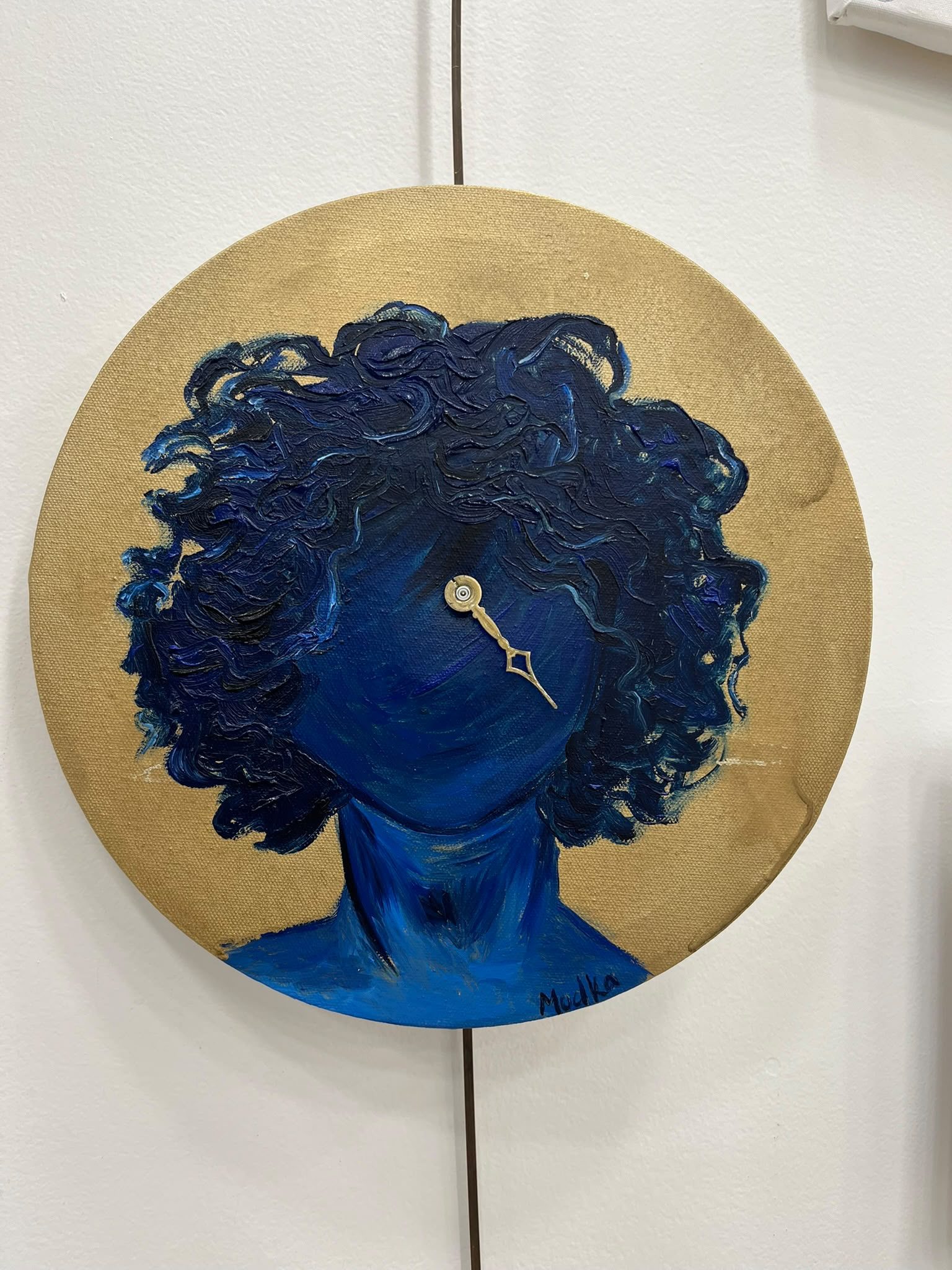 Toile ronde à fond doré : une silhouette bleue aux cheveux bouclés, une aiguille d’horloge posée sur le visage.