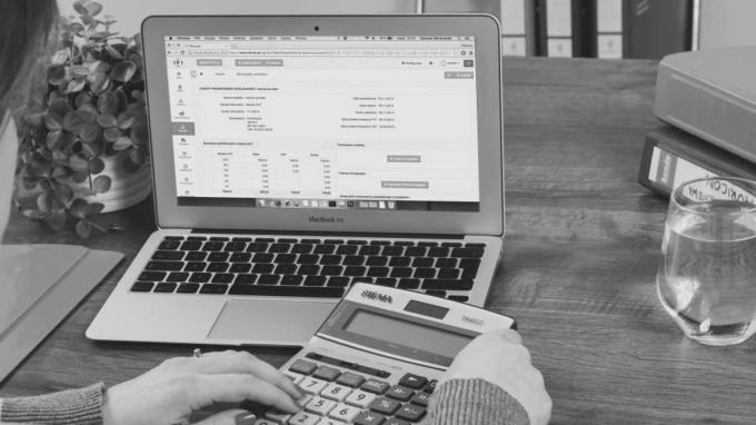 Hands using a calculator beside a laptop showing accounting software