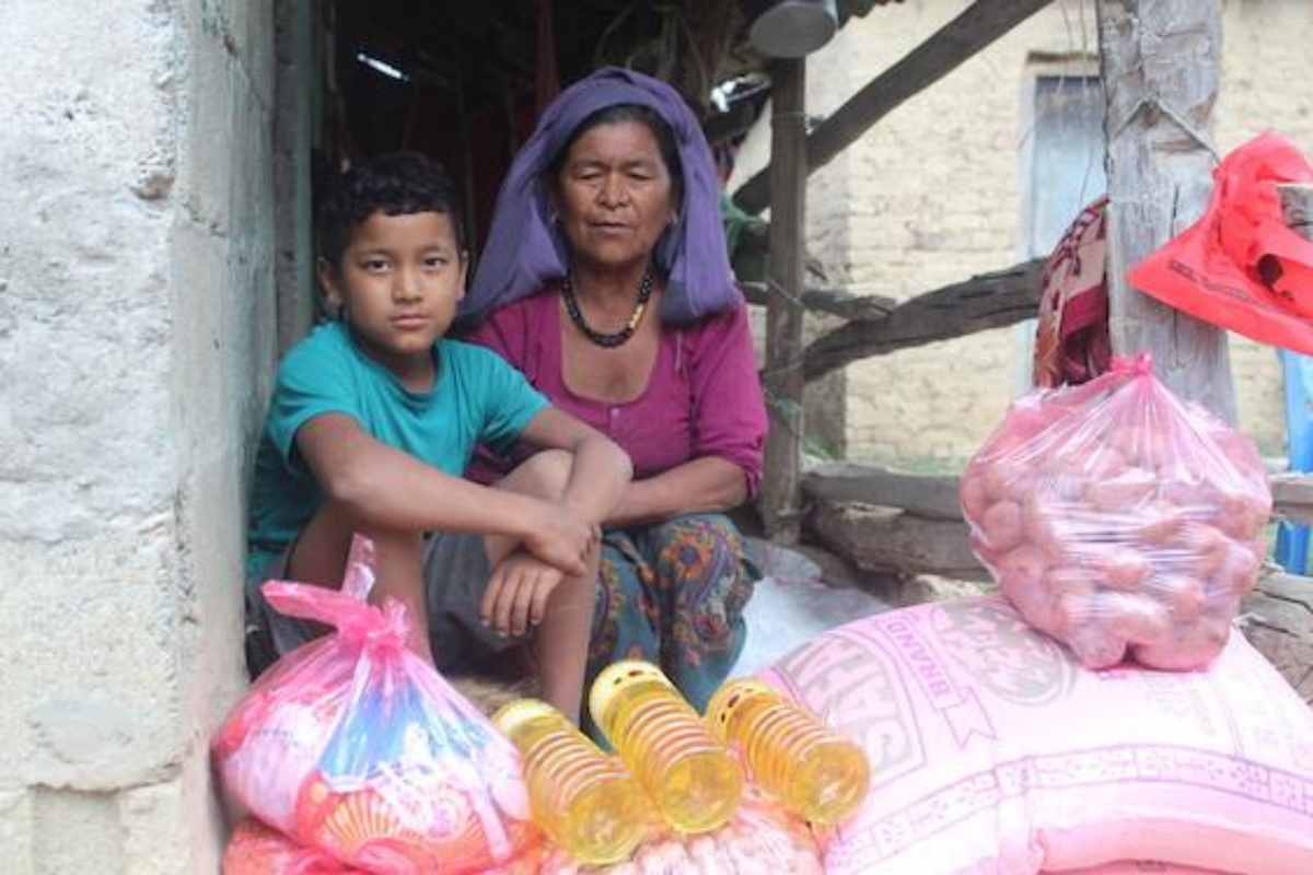 A boy and a woman sitting behind bags of rice, potatoes, and bottles of cooking oil.