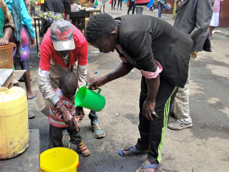 A photo of two men helping a small child wash his hands at a public station in the street