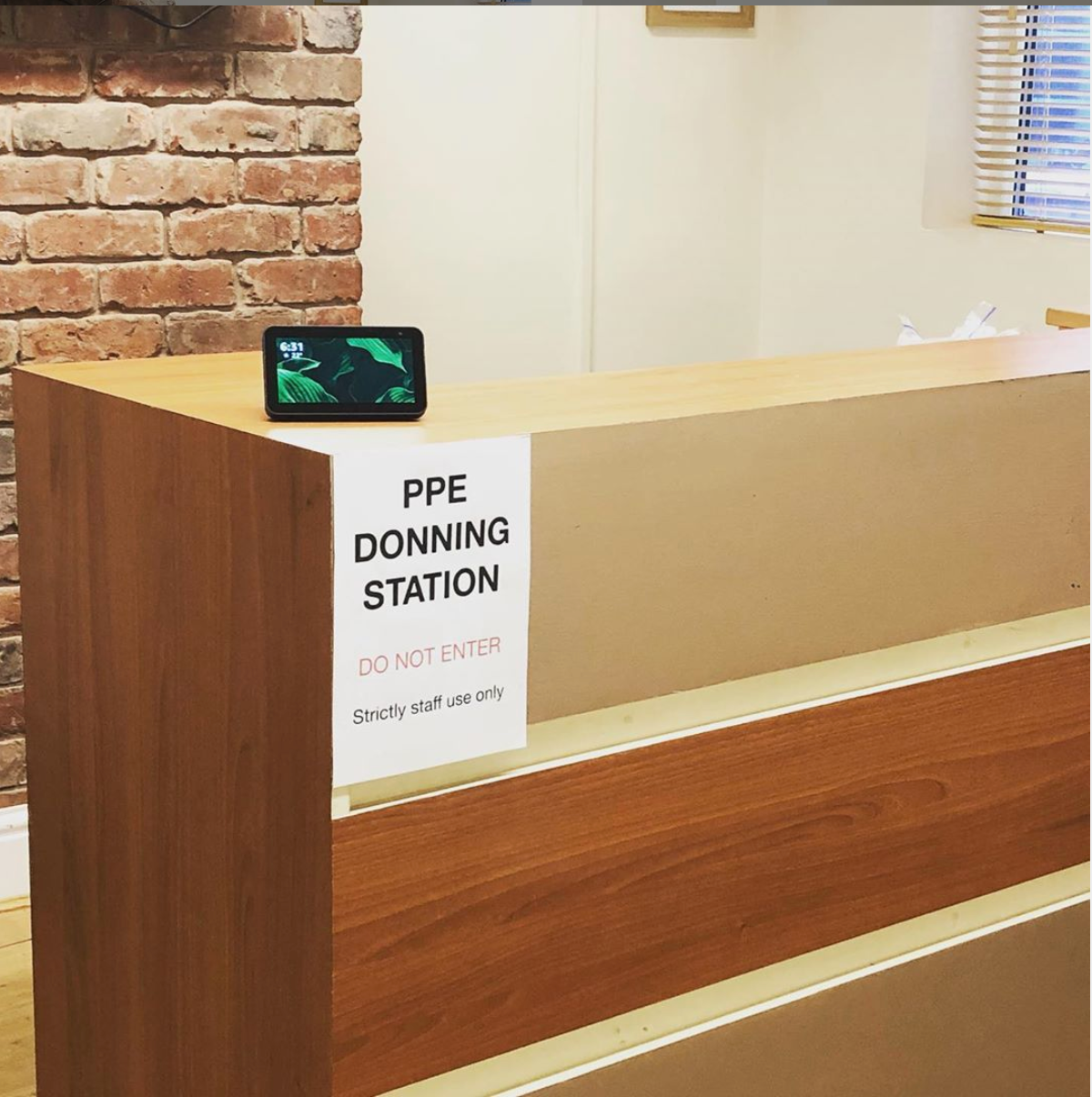 A photo of the PPE donning station at The Village Osteopaths, with a sign advising patients not to enter and a video device so Sean can carry out reception duties remotely