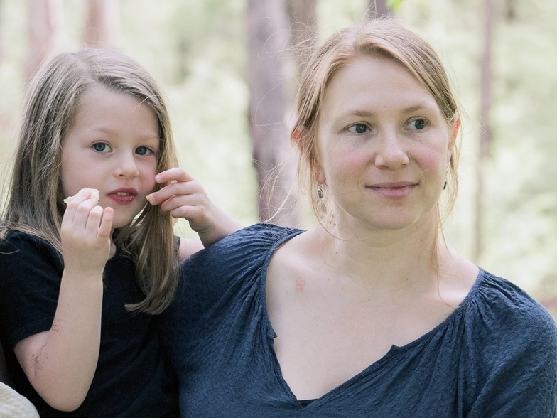 Portrait of osteopath and Cliniko founder Liora Dafner-Beach holding her daughter in a wooded area
