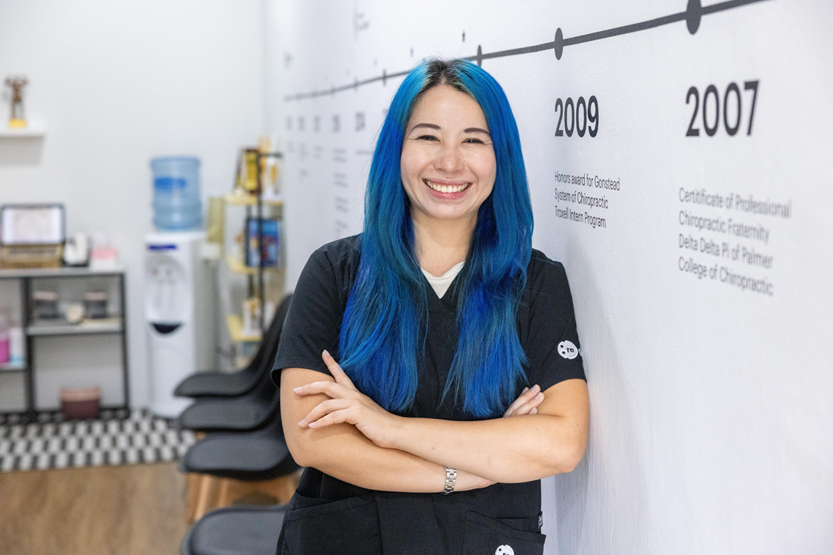 Dr Jenny Li is pictured smiling. The clinic sign is in the background above her head and glimpse of the practice space can be seen behind her.