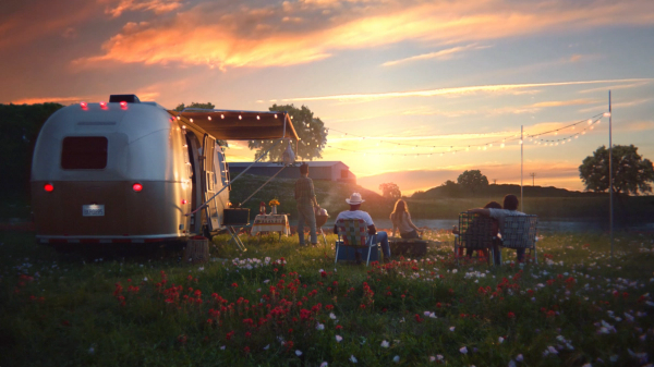 Sunset over the horizon with people sitting outside of a mobile home watching