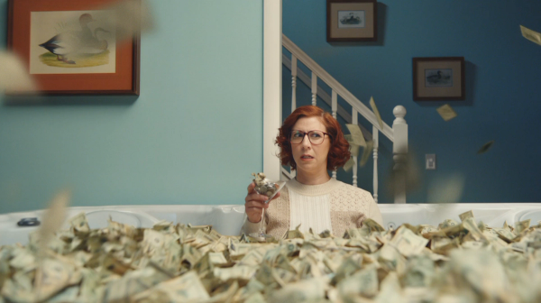 Woman sitting in a room filled with money, holding a martini glass filled with coins