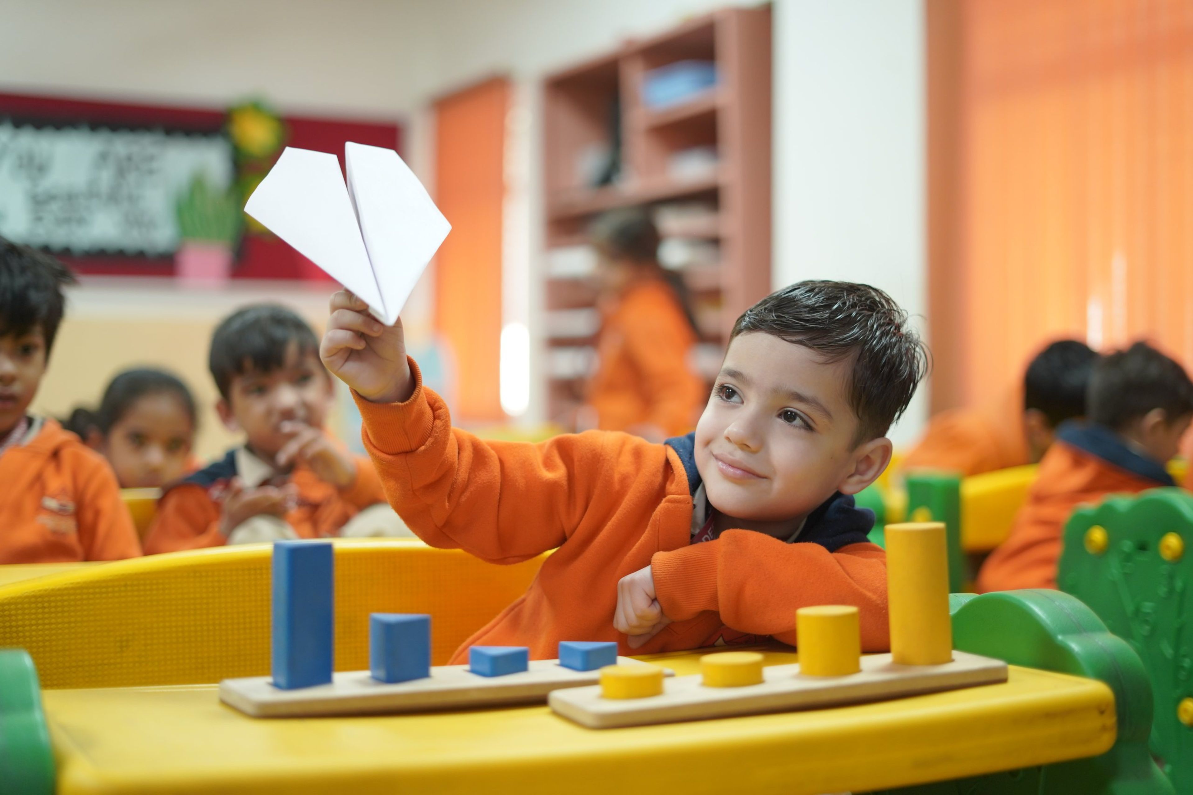 A pre-primary boy holding up a paper plane in class