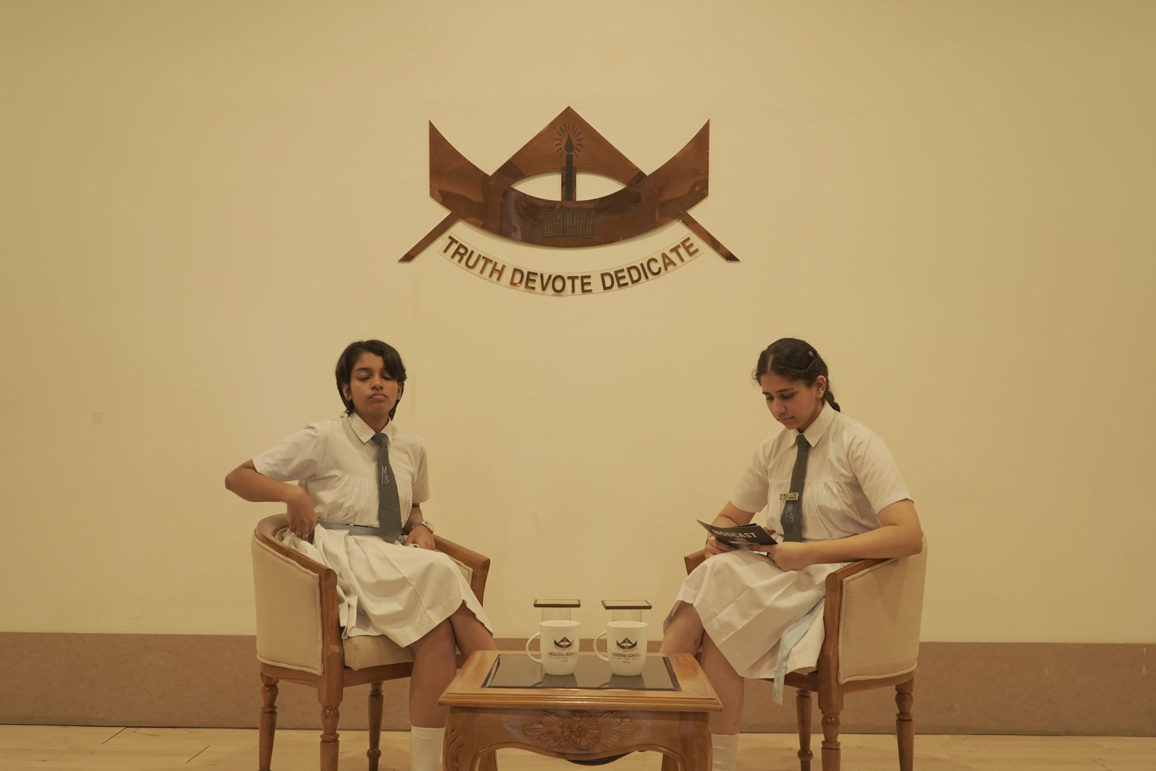 Two students recording the school podcast beneath the school crest