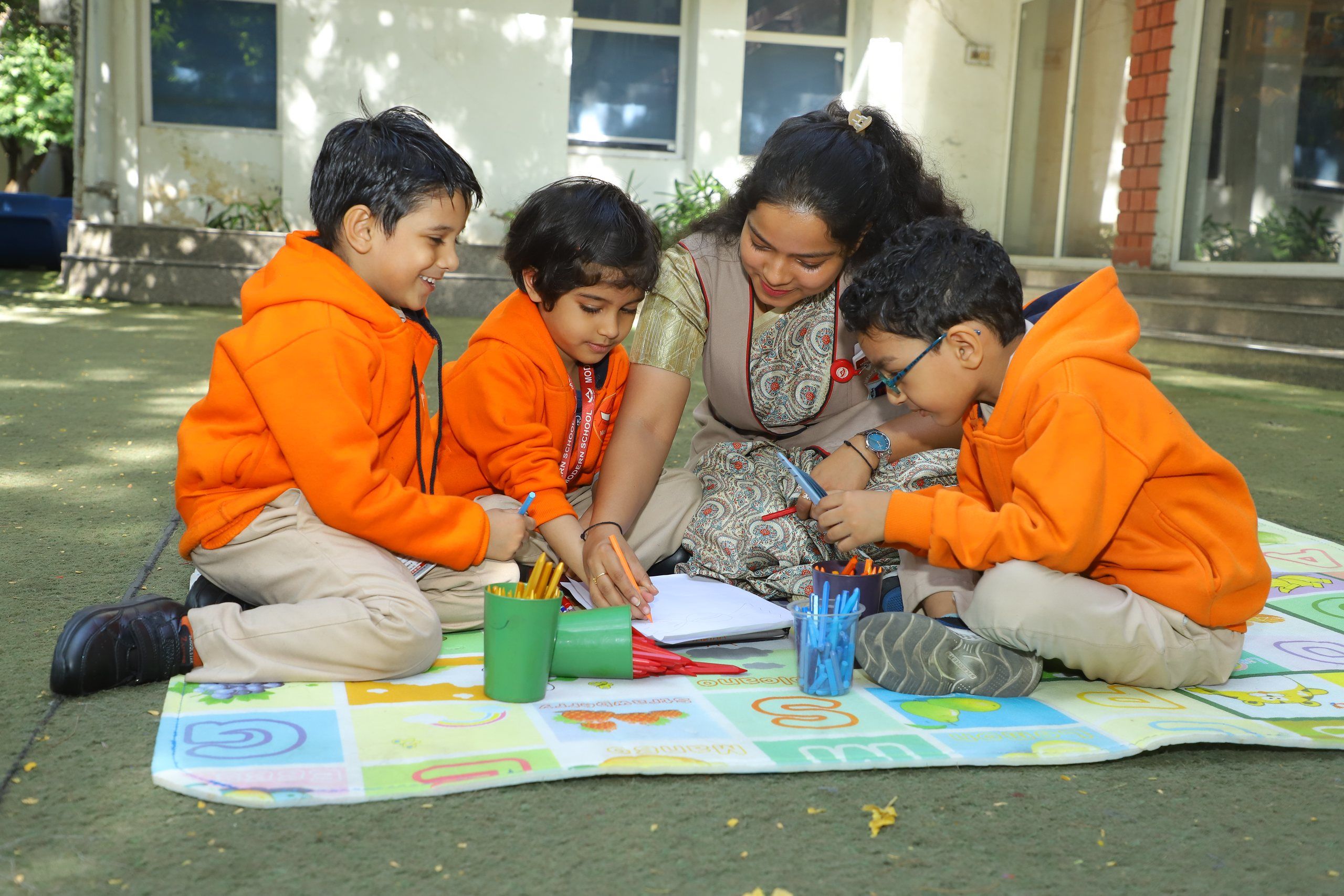 Pre-primary children drawing on a play mat outdoors with their teacher