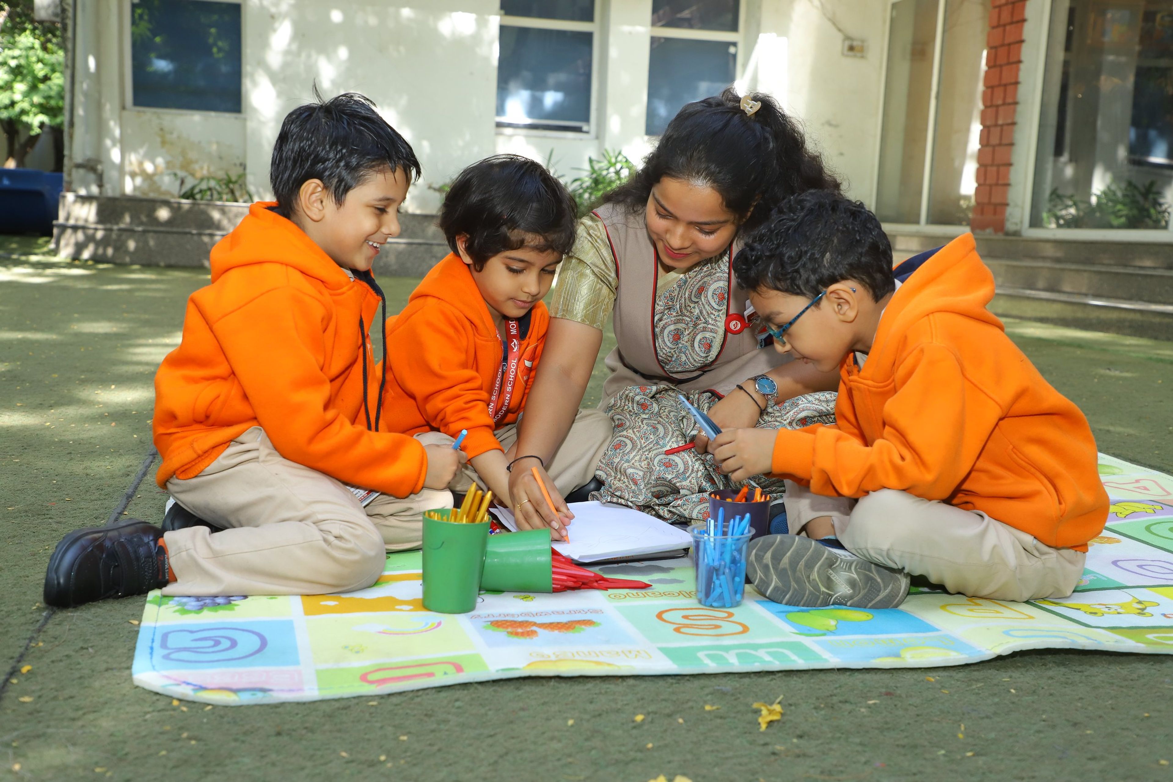 Pre-primary children drawing on a play mat outdoors with their teacher
