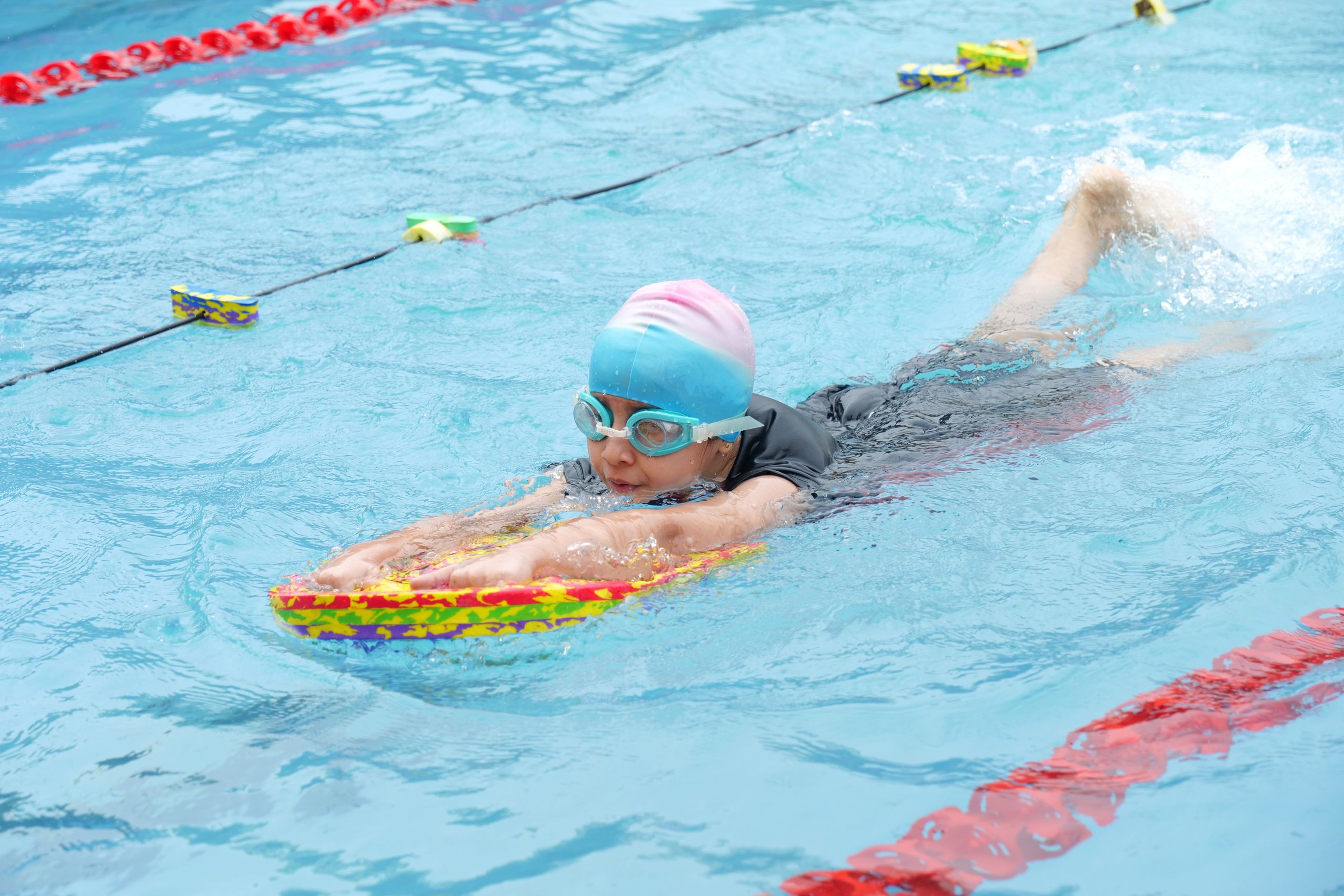 A young swimmer with a kickboard in the school pool