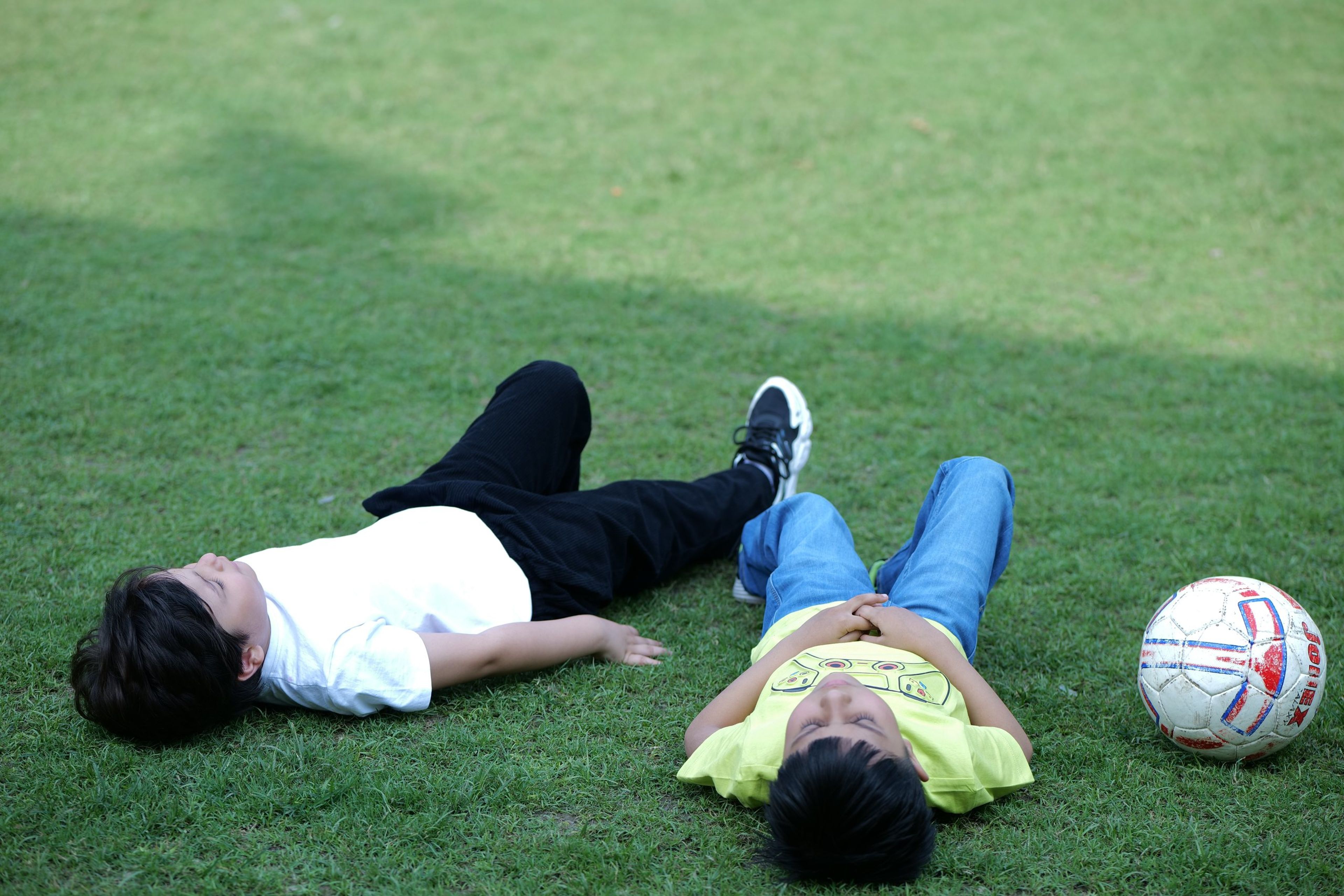 Two students resting on the grass beside a football