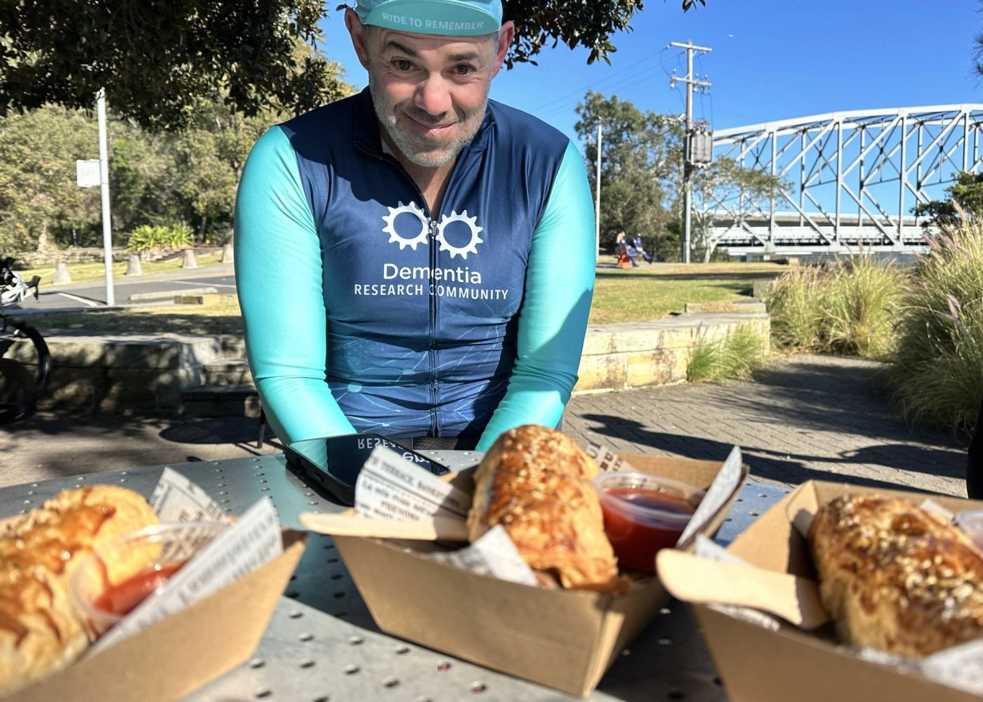 Three pork and fennel sausage rolls in takeaway boxes on a table at Brooklyn, bridge behind