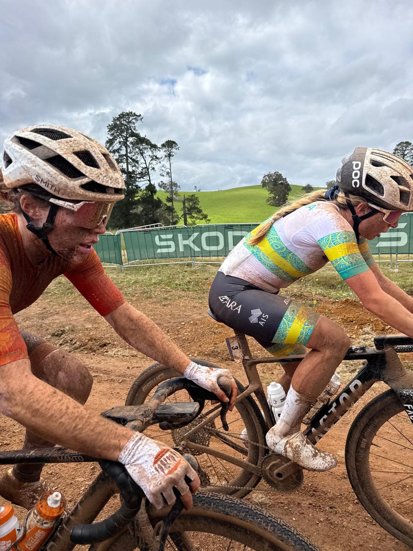 Two mud-caked riders on the Nannup gravel, one in Australian champion’s kit, green hills behind