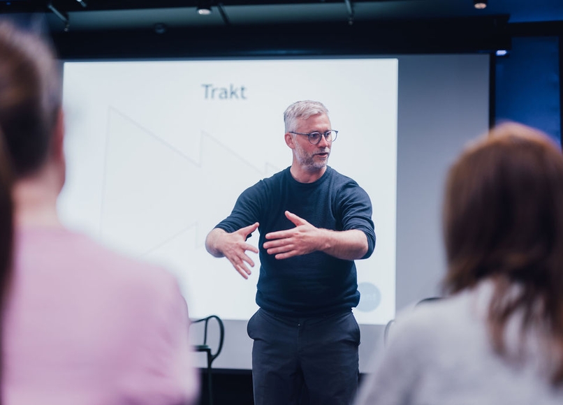 a man is giving a presentation to a group of people in front of a projector screen .