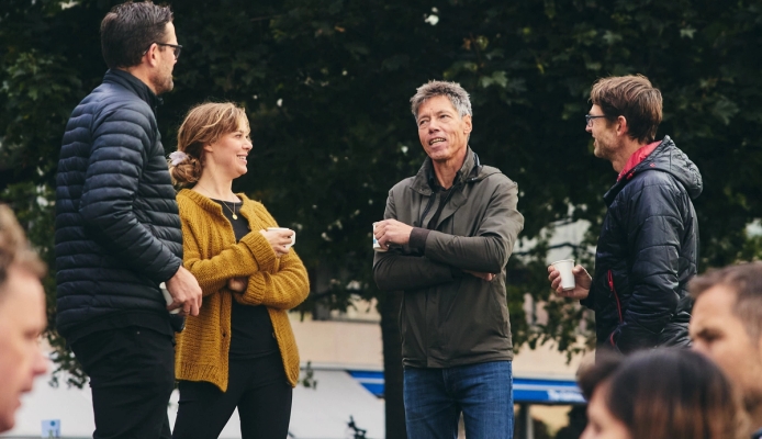 a group of people are standing in a park talking to each other .