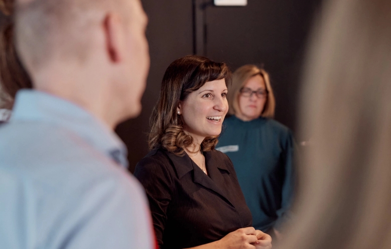 a group of people are standing around a table talking to each other .