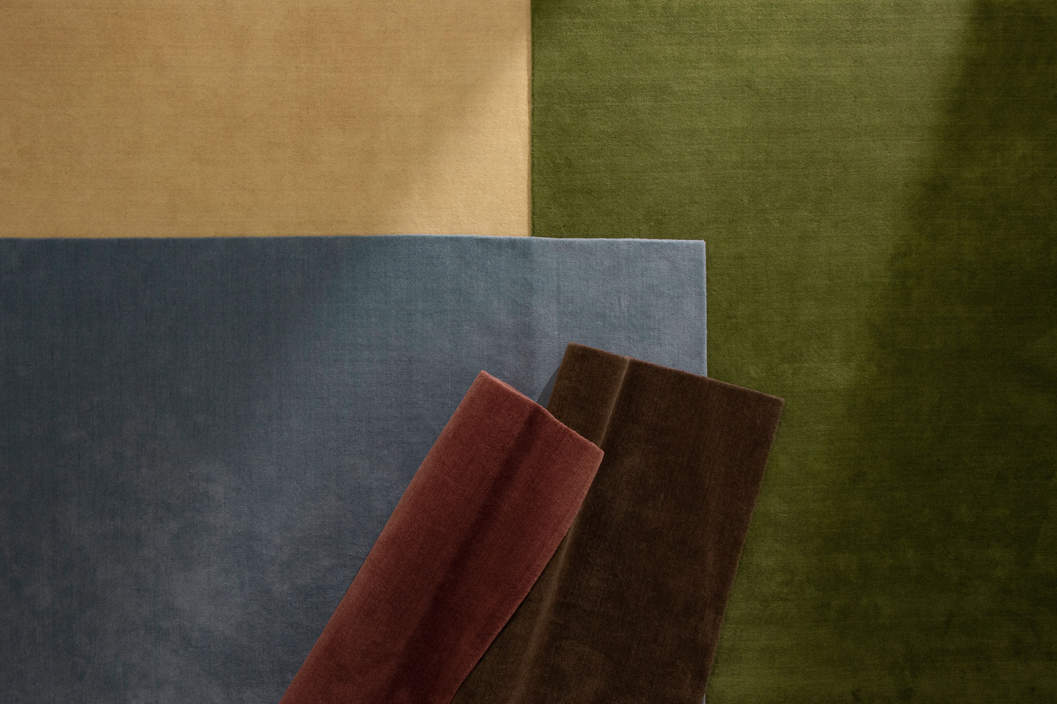 Stack of solid-color wool rugs in tan, olive green, blue, burgundy, and dark brown