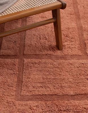 Close-up of the Sybil washable rug in Cinnabar under a wooden chair