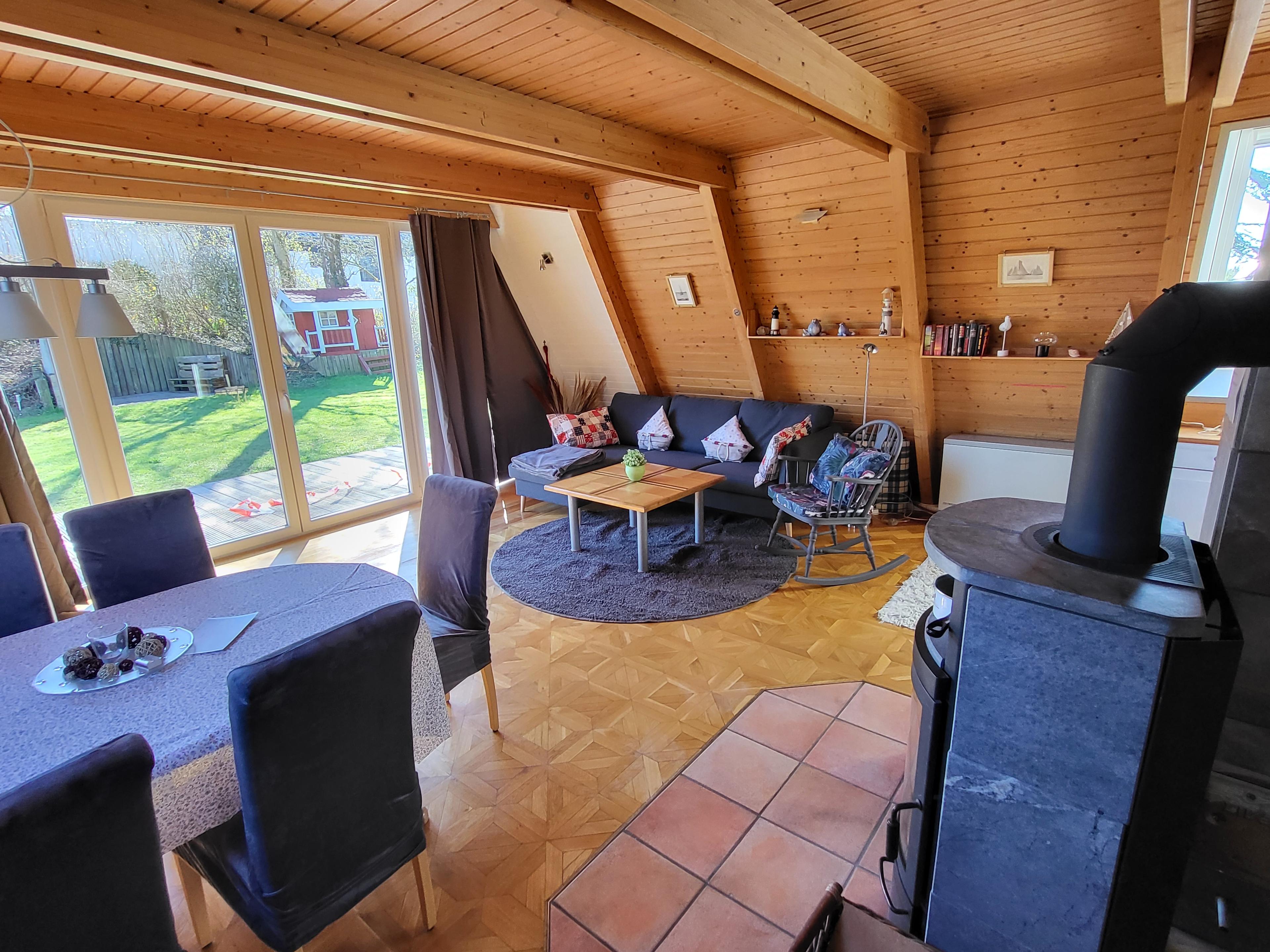 Wohnzimmer mit Holzwänden, Esstisch, Sofa und Blick auf Rasen im Garten.