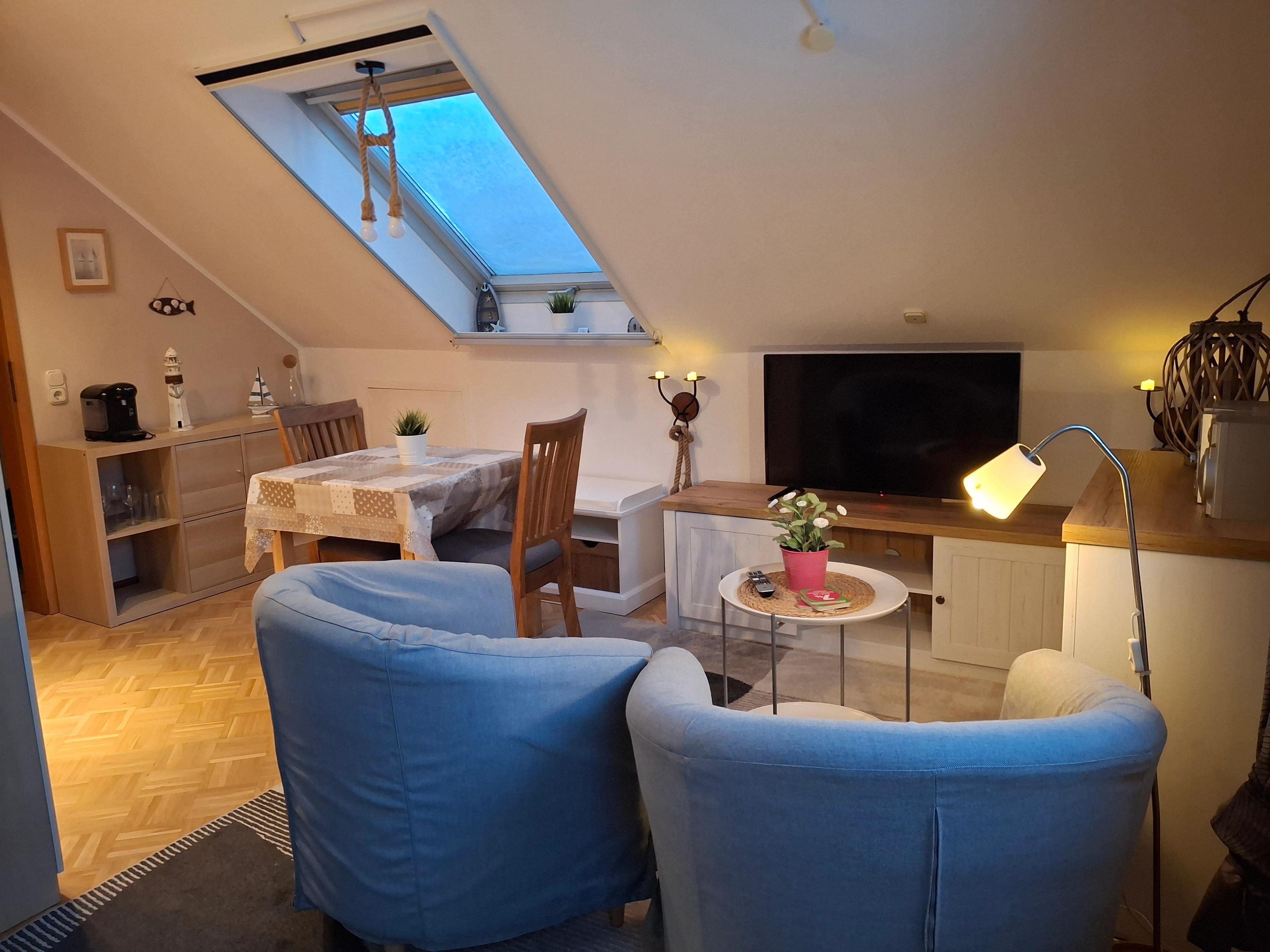 Wohnzimmer im Dachgeschoss mit Sessel, Tisch, Dachfenster und Holzmöbeln.